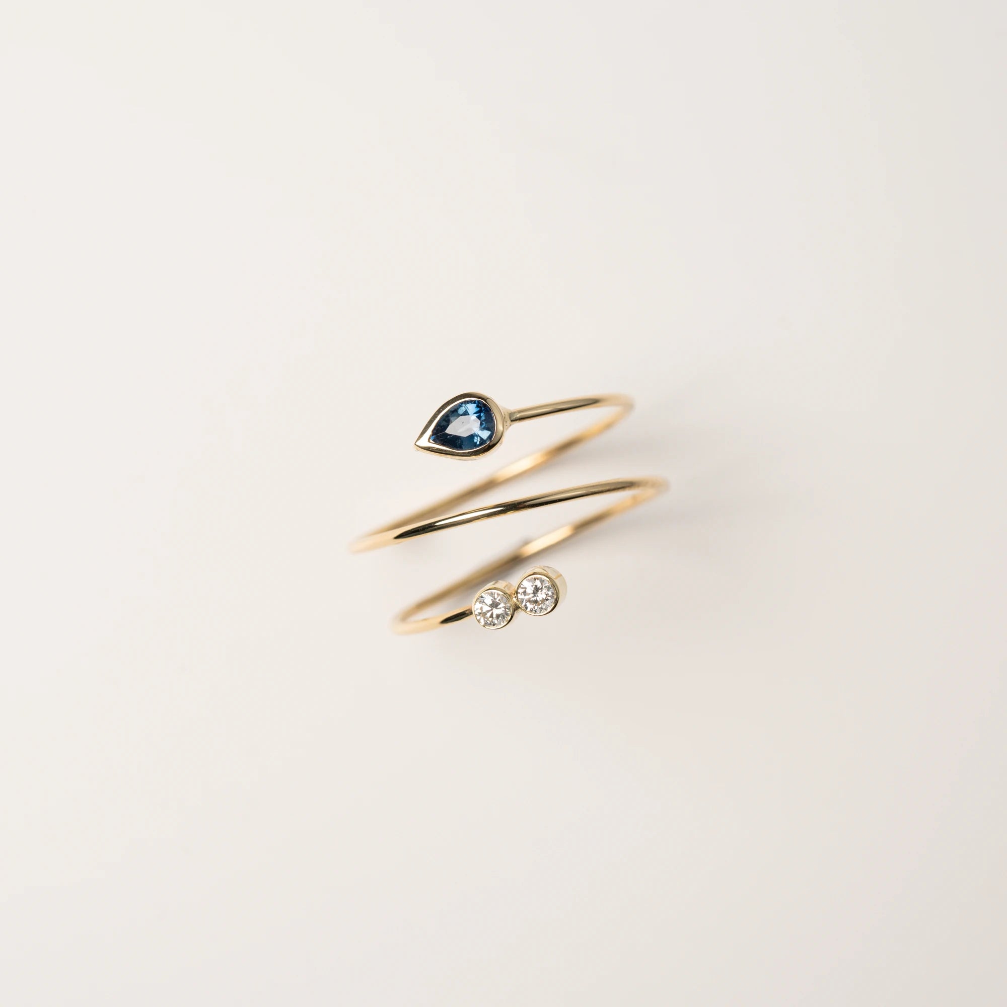 Produktfotografie des Gelbgoldrings Twisted, der an eine Spirale erinnert und als Blickfang zum Abschluss einen Saphir in Tropfenform und zwei Brillanten verbaut hat