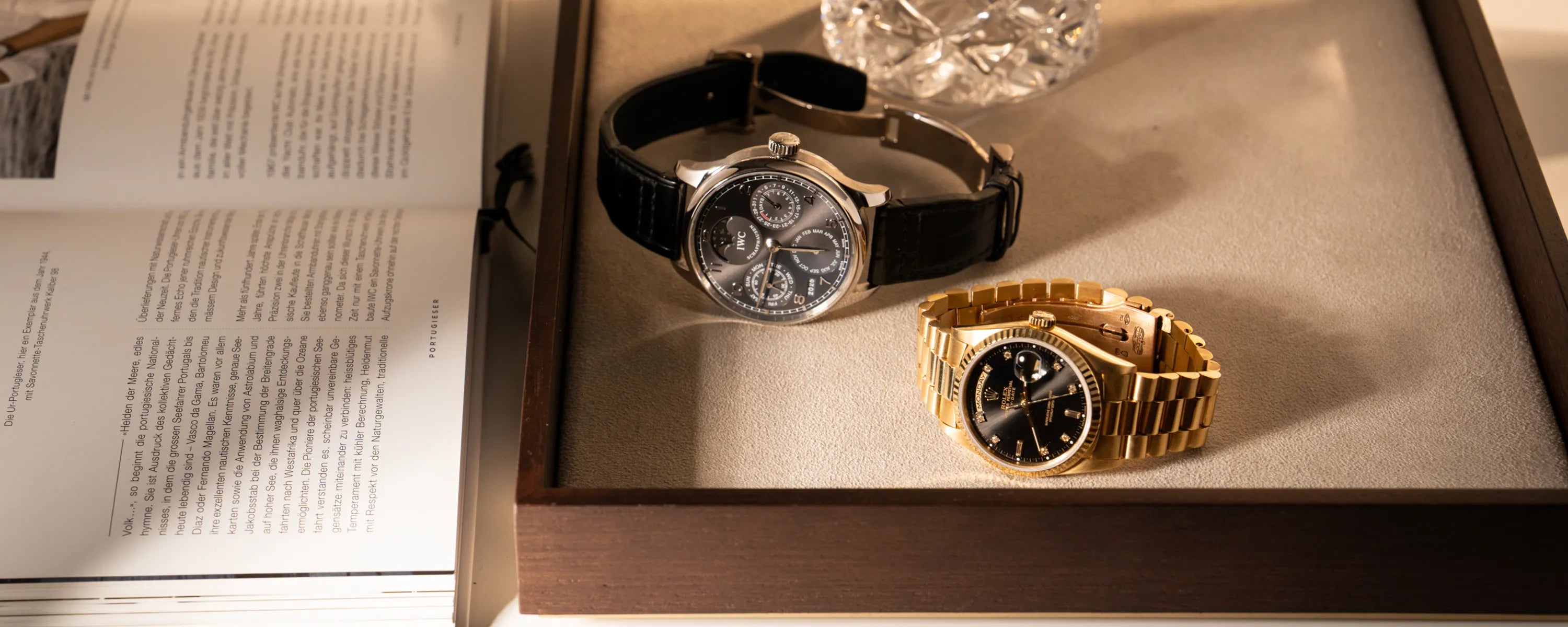 Fotografie eines Juweliertablets, worauf eine Rolex Day Date 36 der Referenz 18238 mit einem schwarzen Diamant-Zifferblatt und einem IWC Portugieser Perpetual Calenders in Weißgold mit einem anthrazit-farbenen Zifferblatt liegen