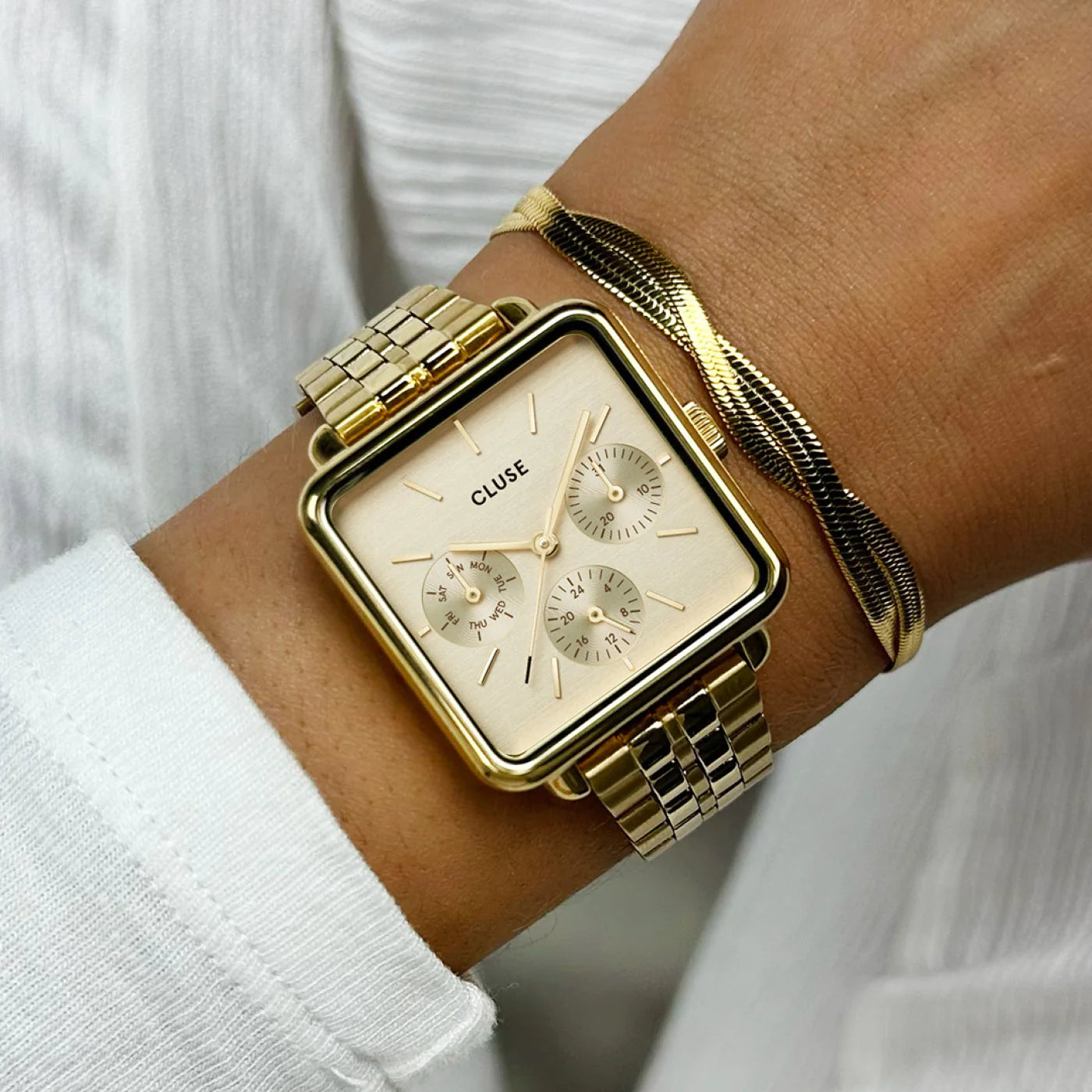 Frau trägt die Cluse Stahl-Uhr "La Tetragone Multifunction" mit gelbgoden-farbigen Gehäuse und Zifferblatt mit drei Sub-Dials an ihrem Handgelenk