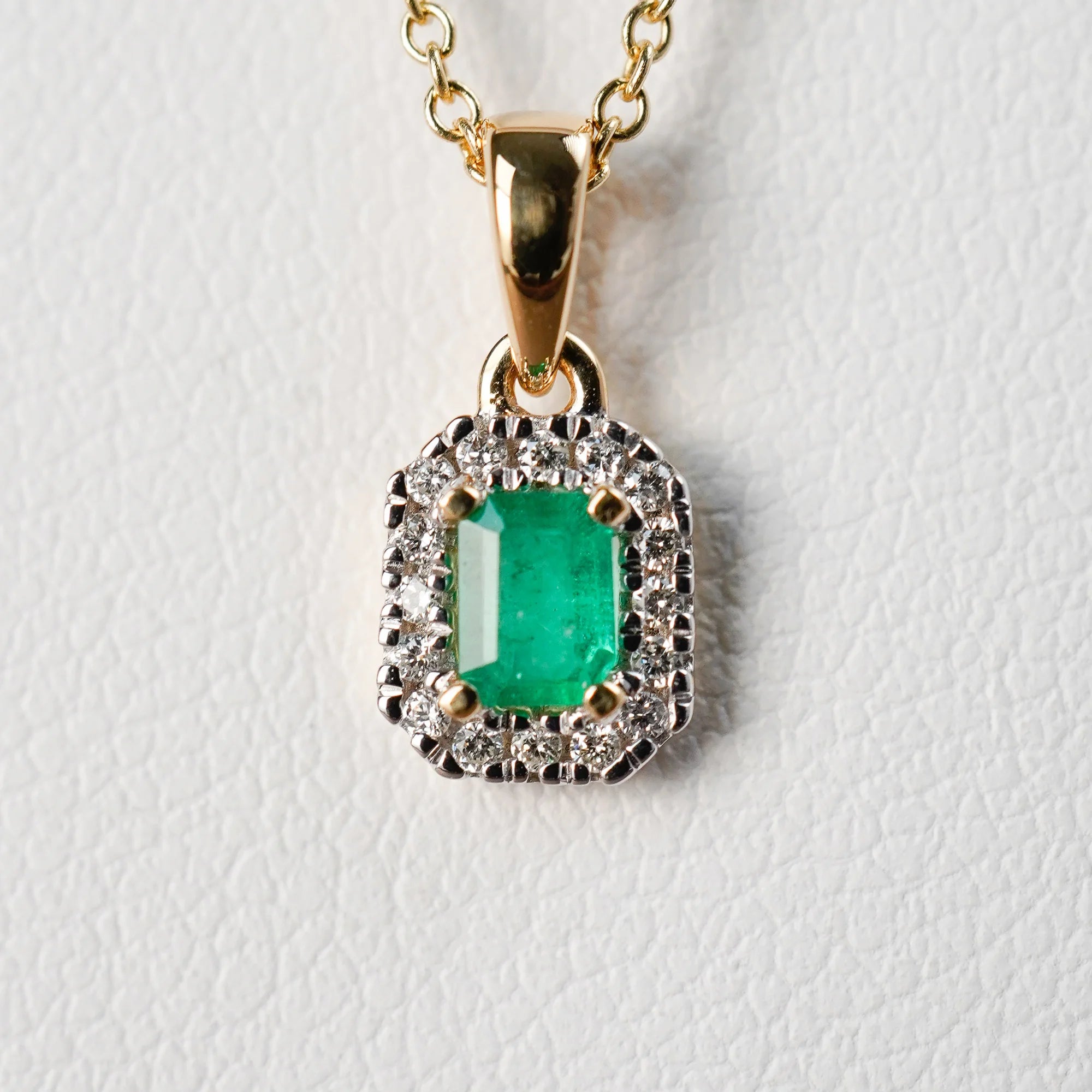 Detailaufnahme des Anhängers mit einem zentralen Smaragd mit einer kräftigen grünen Farbe, der von kleinen Diamanten umrandet ist, von der Smaragd-Brillant-Kette aus der Schmuckatelier Lang Collection