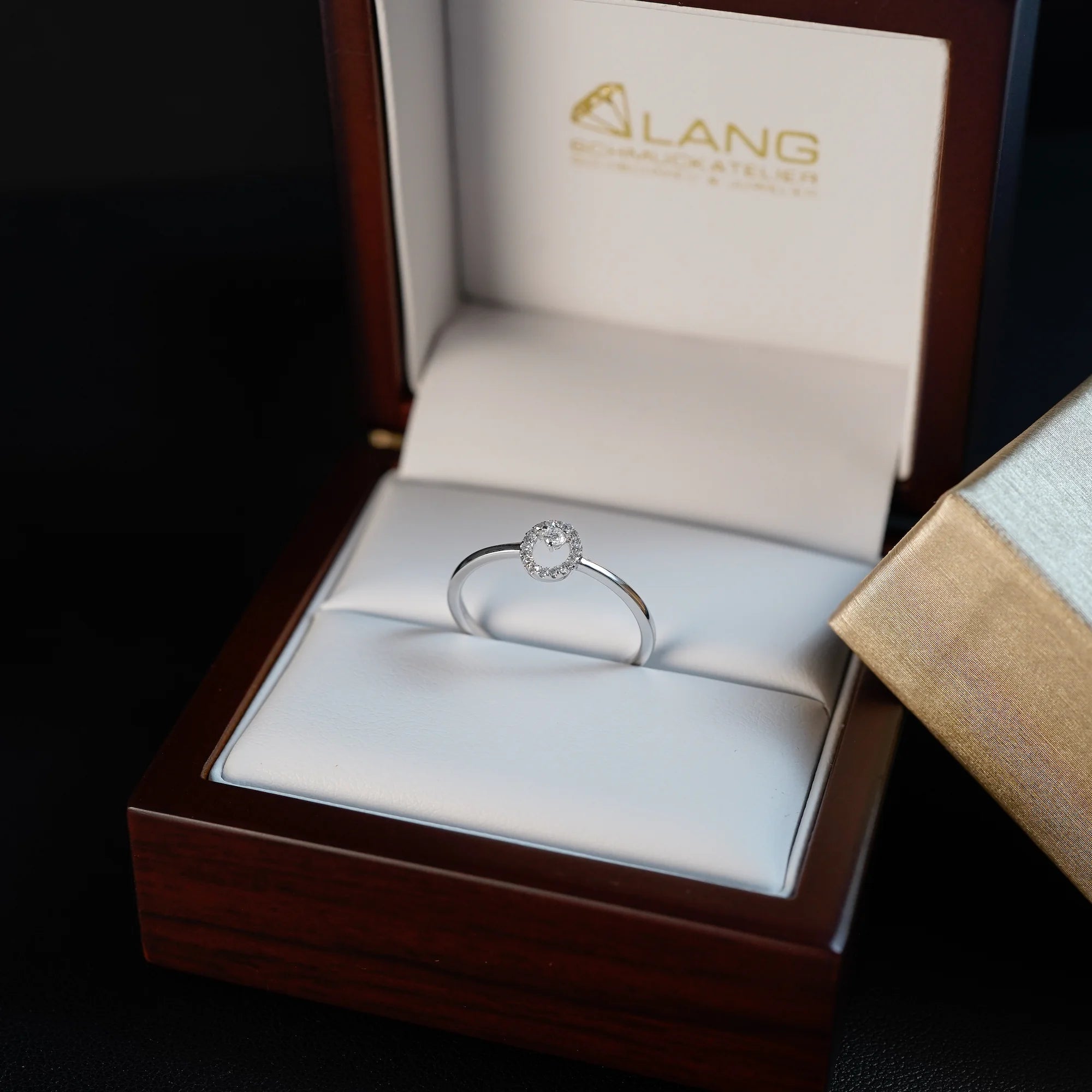 "Fine Oval" Verlobungsring aus Weißgold, der mit einem ovalen Diamantkranz verziert wurde, liegt in der Schmuckatelier Lang Verpackung