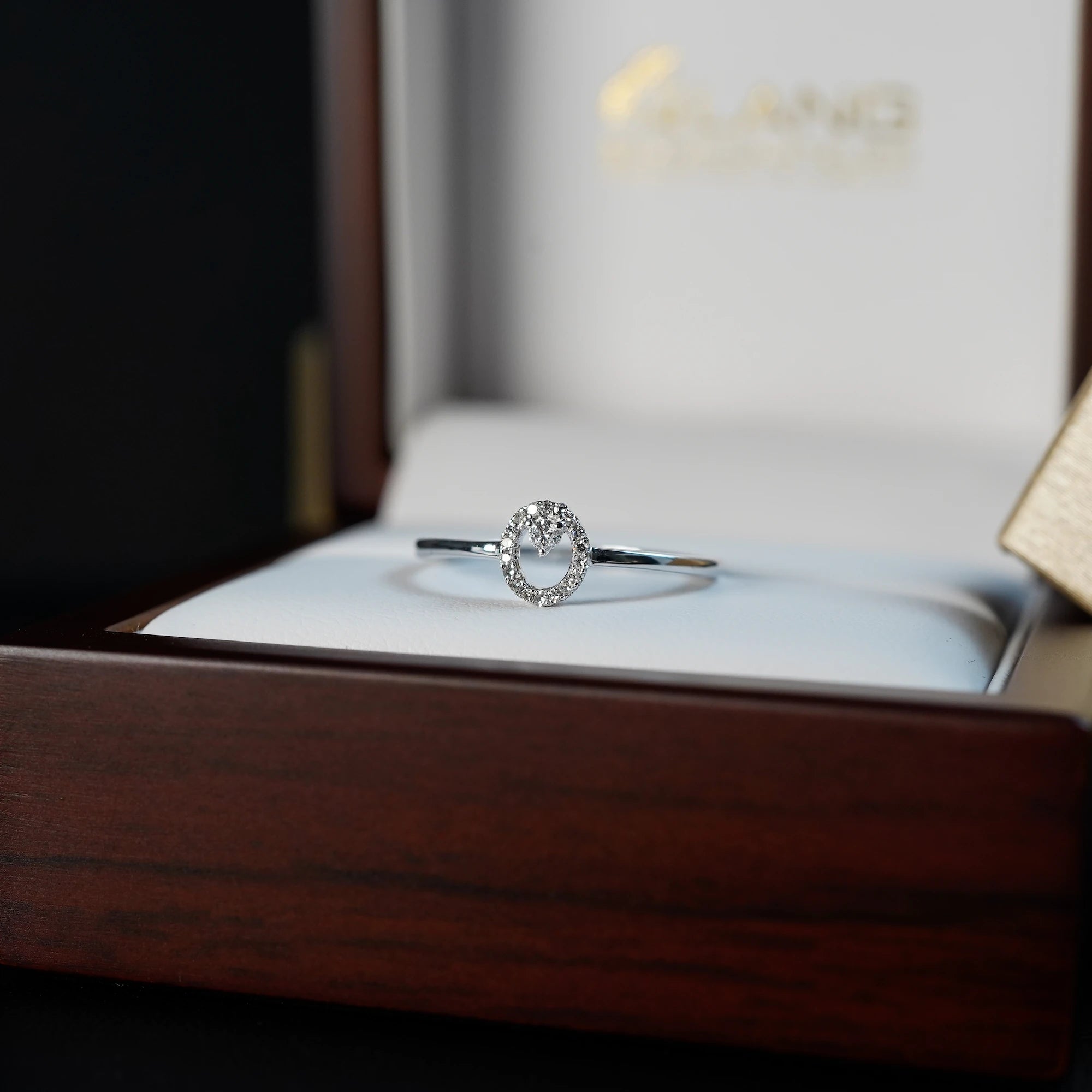 "Fine Oval" Verlobungsring aus Weißgold, der mit einem ovalen Diamantkranz verziert wurde, liegt in der hölzernen Verpackung