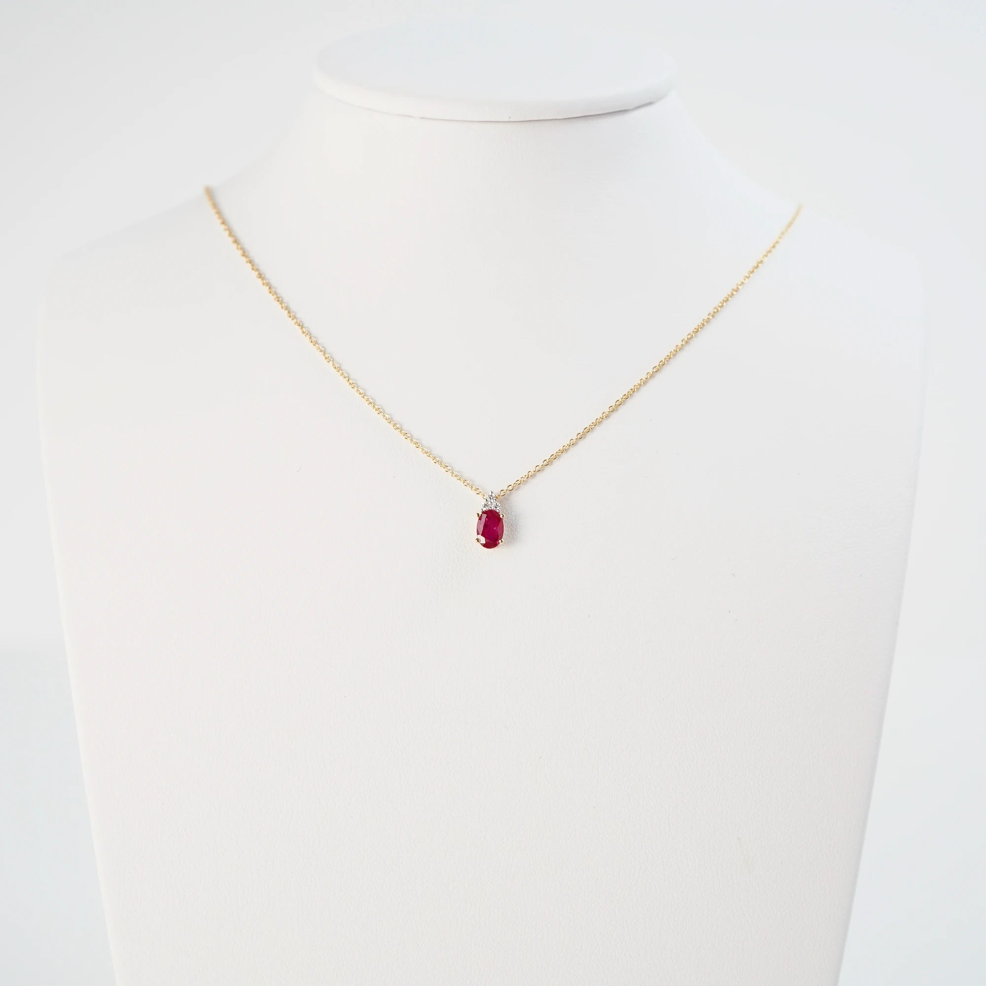 Rubin Collier aus der Schmuckatelier Lang Collection an einer gelbgoldenen Kette und einem mit Diamant-verzierten, ovalen Rubin-Anhänger wird auf einer Schmuckbüste präsentiert