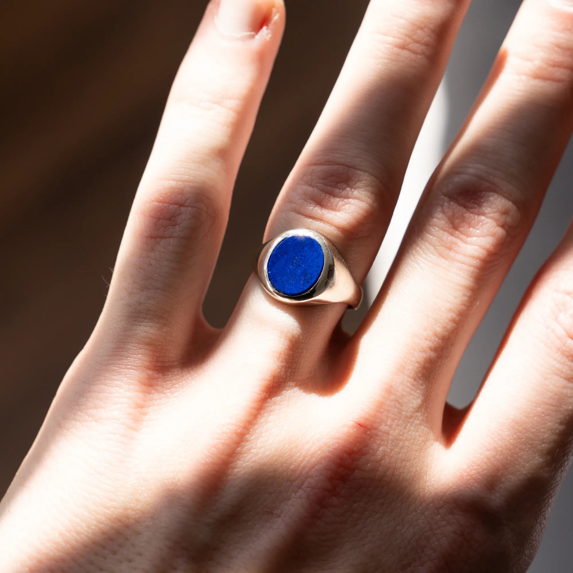 Handgefertigter Siegelring aus 925er Silber mit einem eingefassten, ovalen Lapis Lazuli Edelstein am Ringfinger der linken Hand eines Mannes