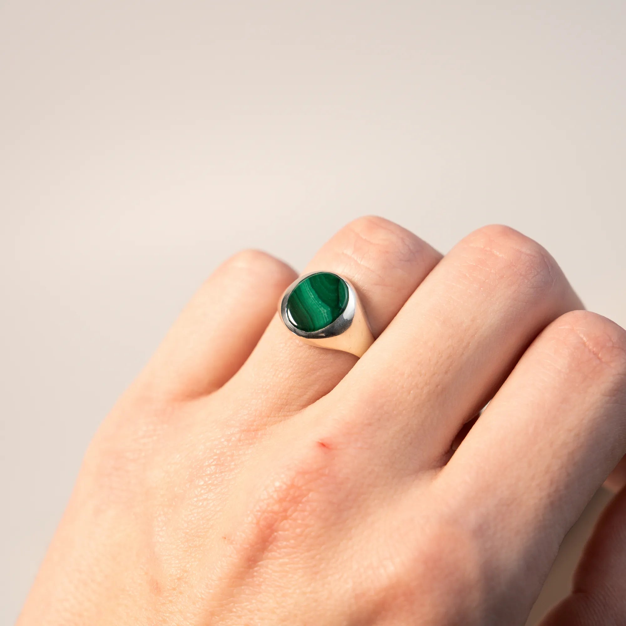 Handgefertigter Siegelring aus 925er Silber mit einem eingefassten, ovalen Malachit Edelstein am Ringfinger der linken Hand eines Mannes