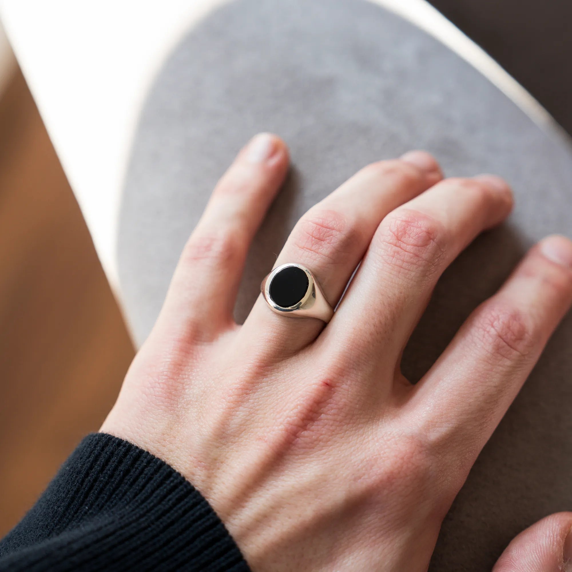 Mann präsentiert den handgefertigten Siegelring aus 925er Silber mit einem eingefassten, ovalen Onyx Edelstein an seinem Ringfinger in die Kamera