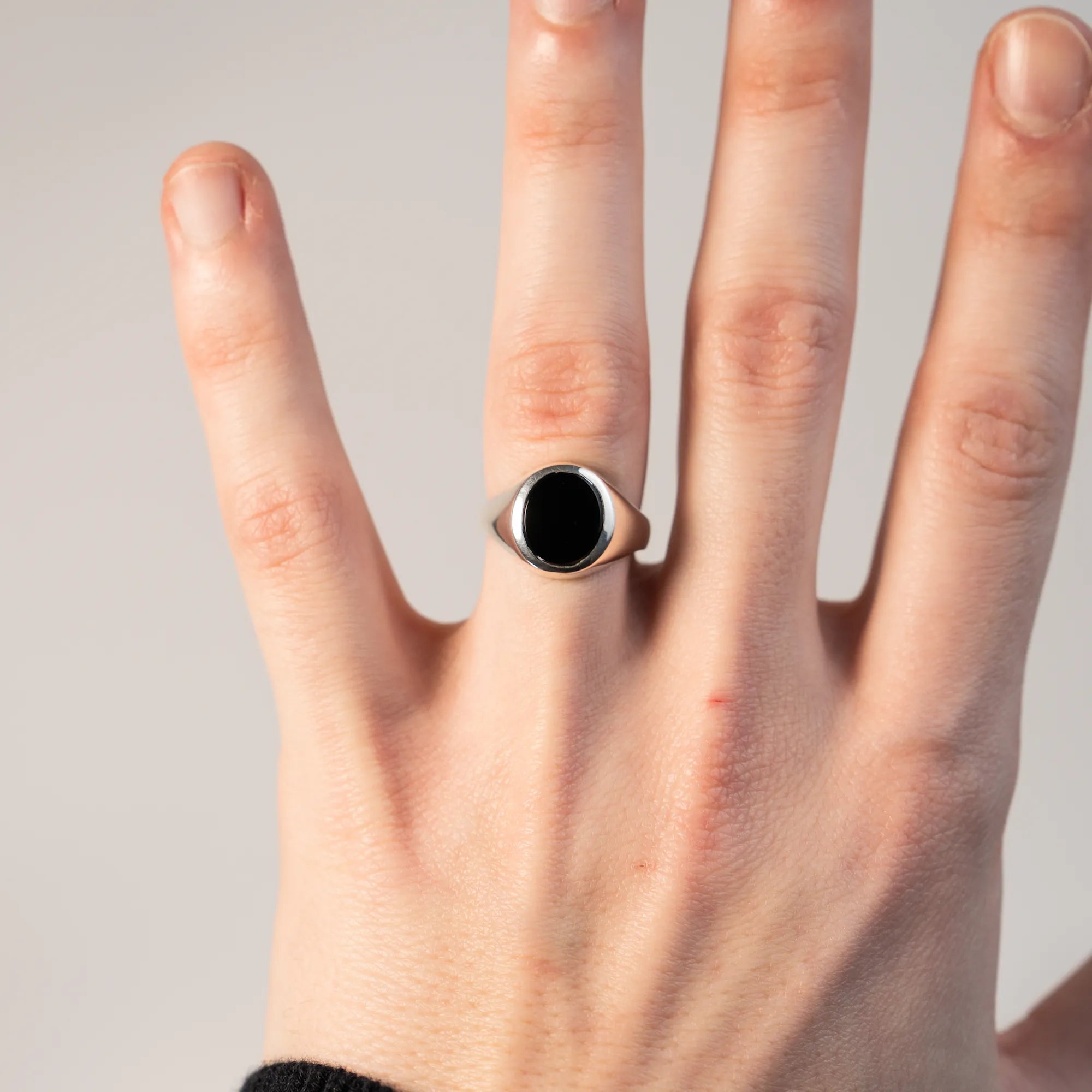 Handgefertigter Siegelring aus 925er Silber mit einem eingefassten, ovalen Onyx Edelstein am Ringfinger der linken Hand eines Mannes