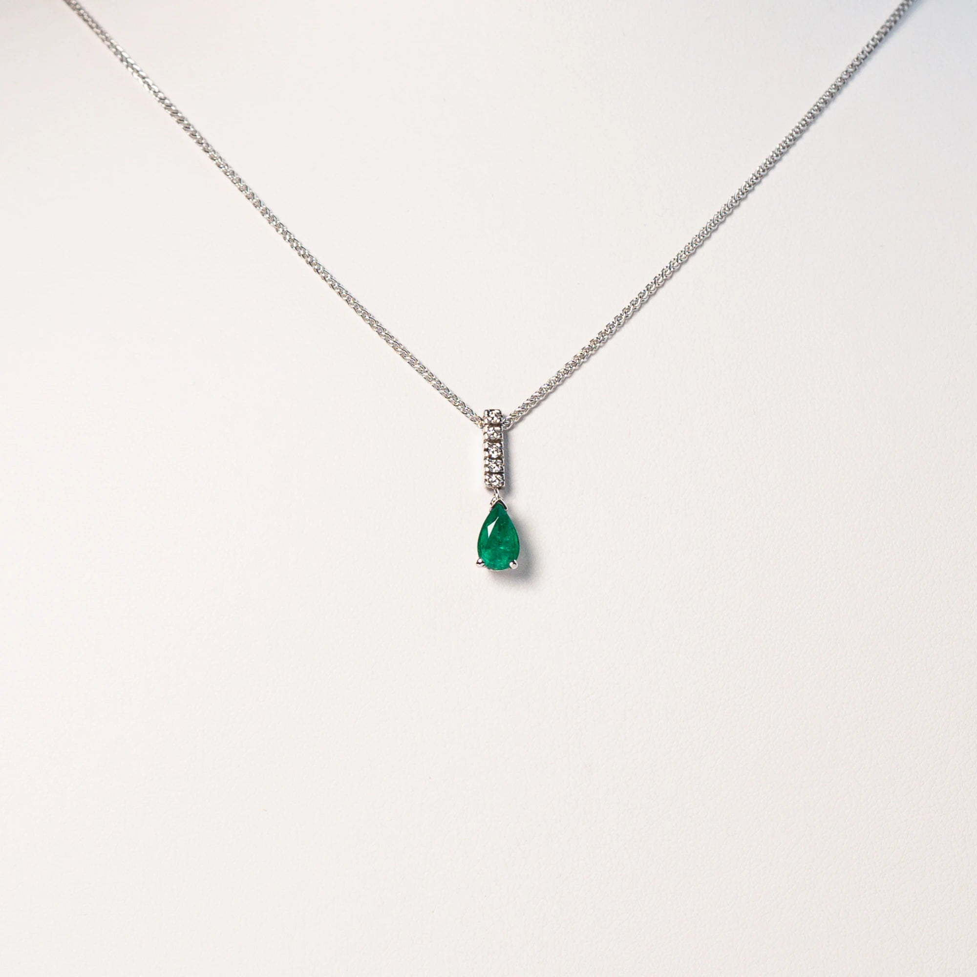 Proukttfoto mit frontalem Blick auf das Smaragd Collier in Weißgold mit einem Anhänger bestehend aus einem Diamant-Steg und einem kräftigen, grünem Smaragd im Tropfenschliff