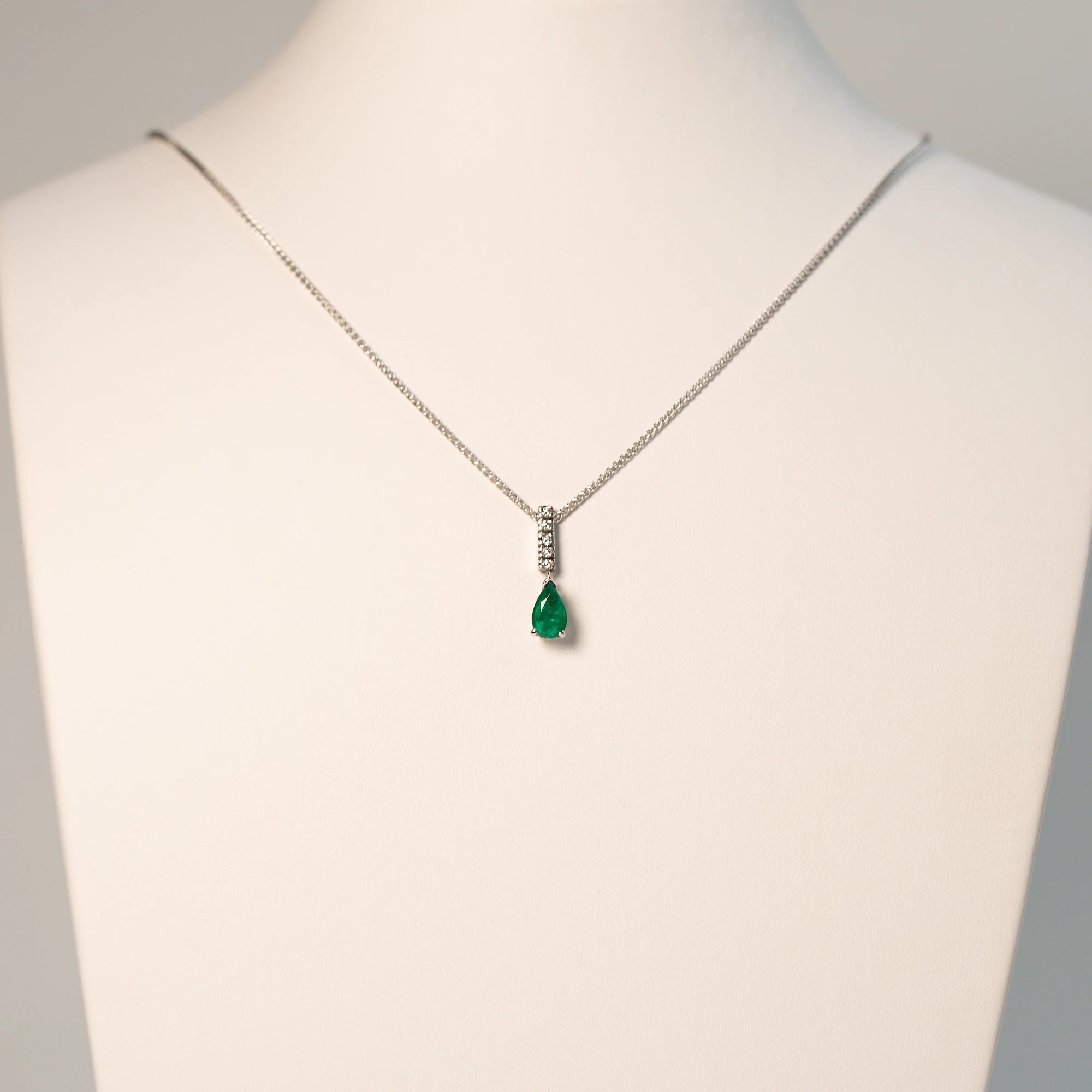 Detailaufnahme des Smaragd Colliers in Weißgold mit einem Anhänger bestehend aus einem Diamant-Steg und einem kräftigen, grünem Smaragd im Tropfenschliff aus der Schmuckatelier Lang Collection - wird auf einer Büste präsentiert