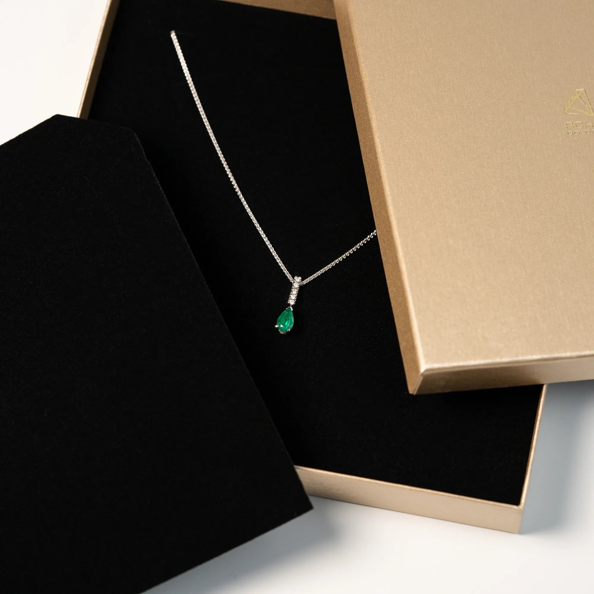 Smaragd Collier in Weißgold mit einem Anhänger bestehend aus einem Diamant-Steg und einem kräftigen, grünem Smaragd im Tropfenschliff aus der Schmuckatelier Lang Collection liegt in der Schmuckverpackung