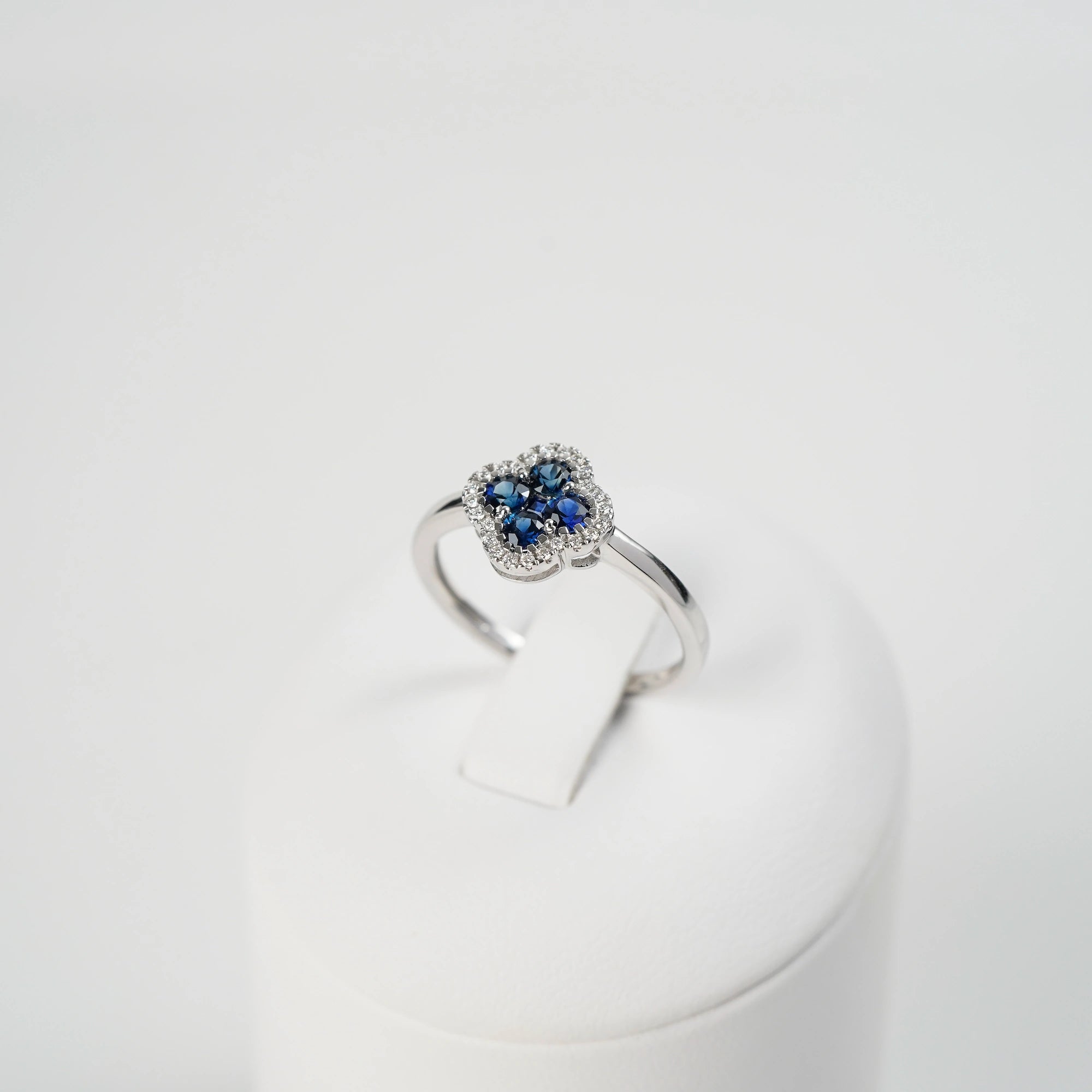 Weißgoldring aus der Schmuckatelier Lang Collection mit einer Verzierung in einer Kleeblatt-Form, bei dem die Saphire durch die kleinen Diamanten umrandet sind, wird auf einem Ringständer präsentiert