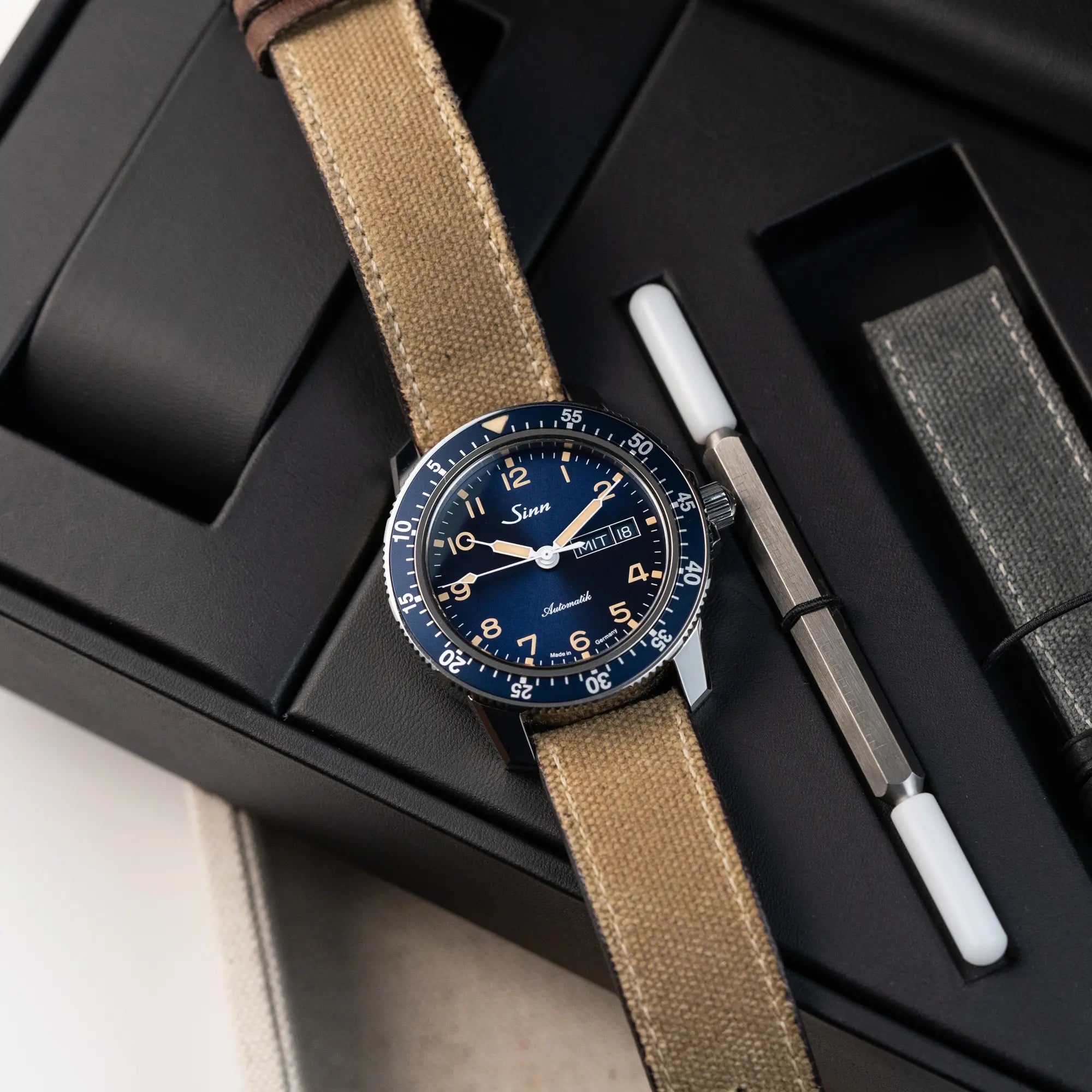 Produktfotografie derder Taucheruhr Sinn Automatik SA in Blau mit beigen Akzenten am Textilband, während die Uhr auf der Uhrenbox liegt