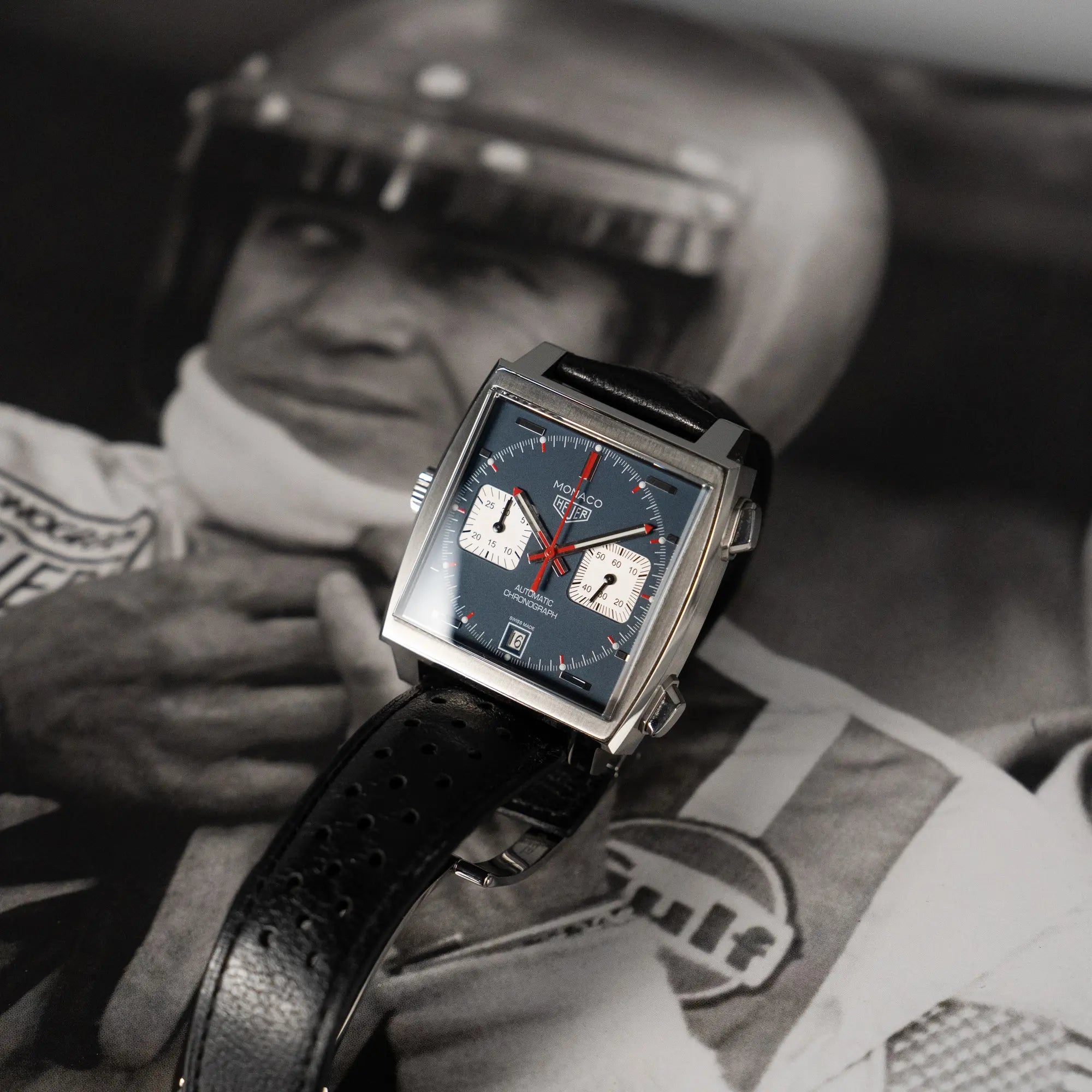 Produktfotografie des Tag Heuer Monaco Calibre 11 Chronographen CAW211P mit dem klassischen blauen Zifferblatt und roten Details auf Ziegern und Indizes mit Steve McQueen als Hintergrund