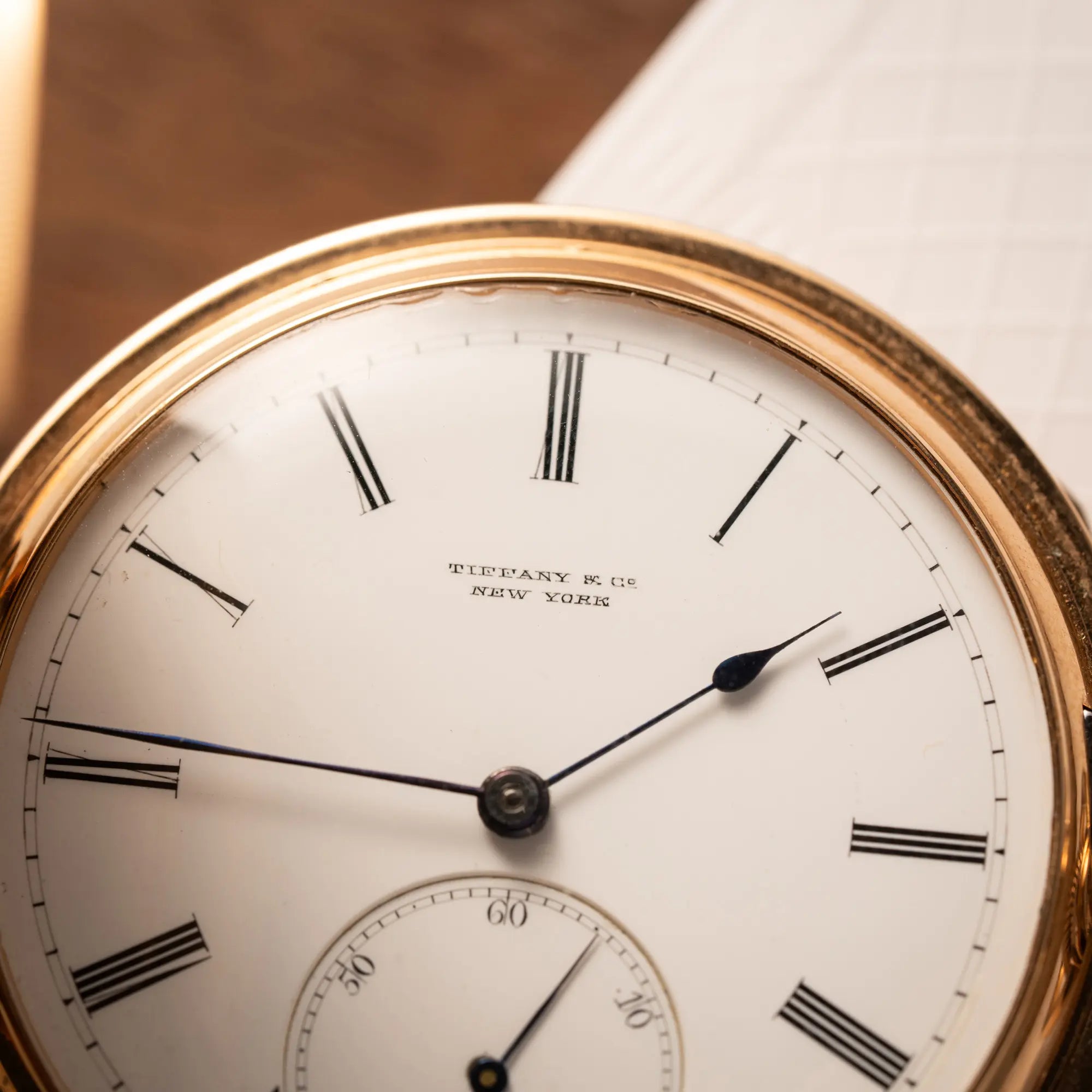 Produktfotografie der Tiffany & Co Savonette Taschenuhr aus 18k Gelbgold mit weißem Zifferblatt und römischen Indizes mit Fokus auf dem "Tiffany & Co New York" Schriftzug