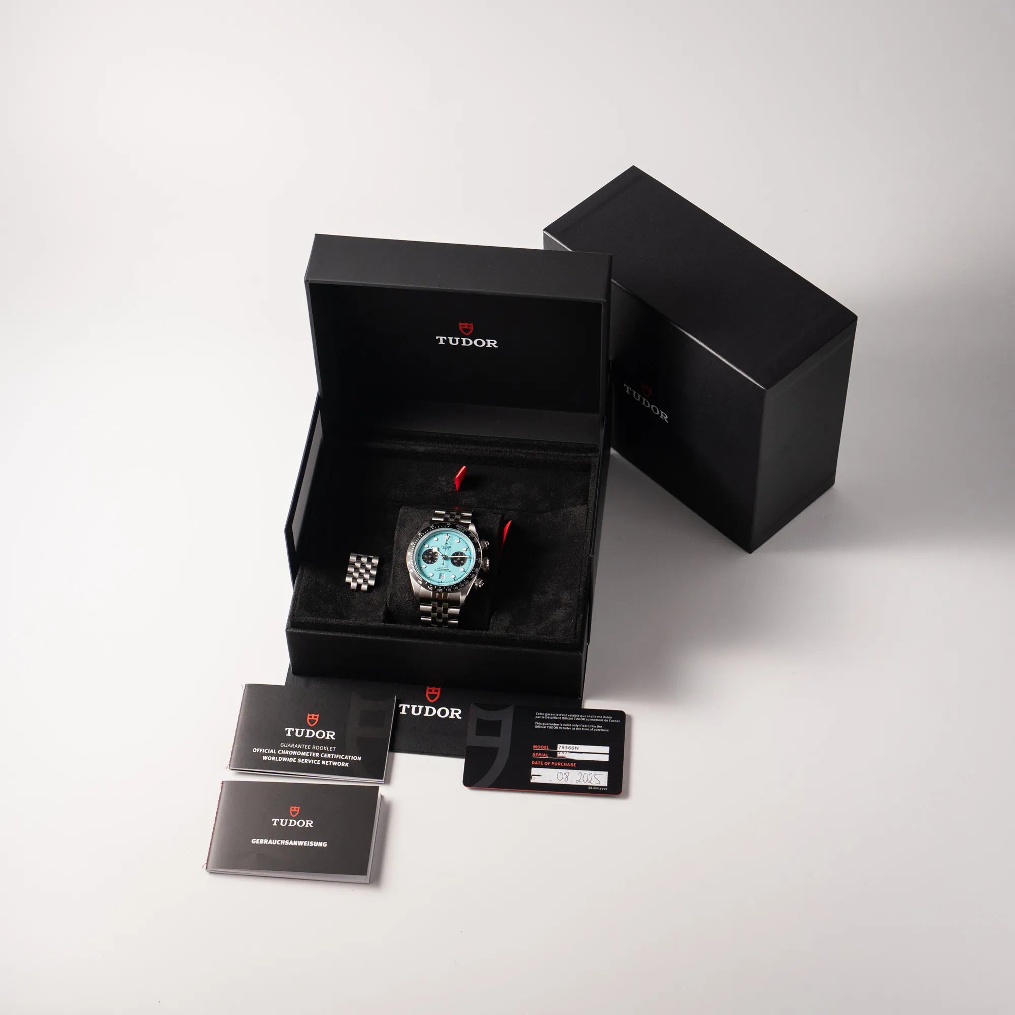 Lieferumfang zugehörig zu der Tudor Black Bay Chronograph Flamingo mit dem türkis-blauen Zifferblatt und schwarzer Lünette mit Zähler-Skala, bestehend aus Box mit Umkarton, originaler Garantiekarte und allen Booklets