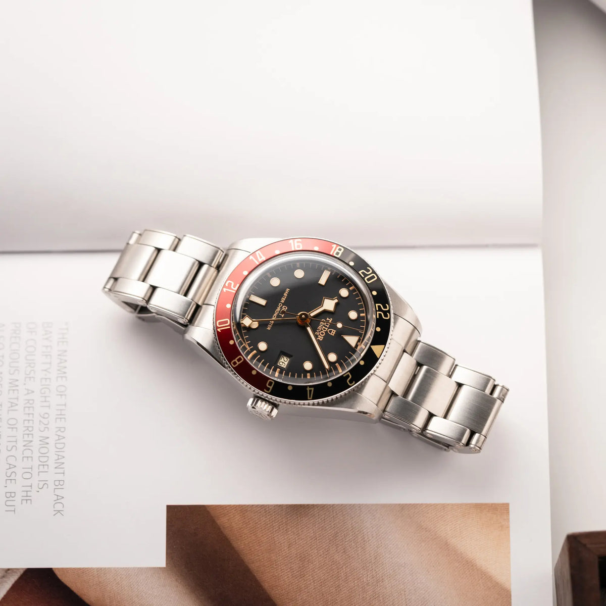 Tudor BlackBay GMT Coke der Referenz 7939G1A0NRU mit der schwarz-roten Lünette und bronzefarbenen Details am Edelstahlarmband liegt flach auf einem Uhrenbuch