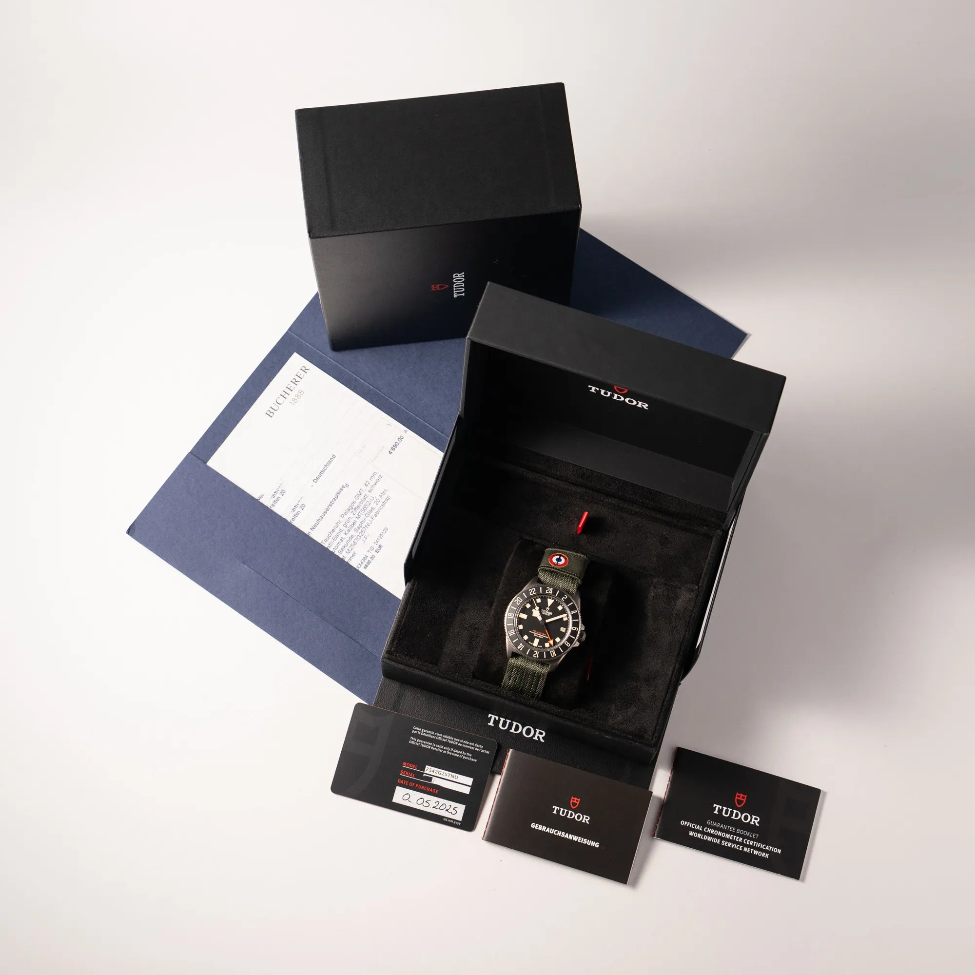 Lieferumfang zu der Tudor Pelagos GMT Military der Referenz M2542G257NU-0002 mit Titan-Gehäuse und schwarzem Zifferblatt an einem olivgrünen Nato-Strap, betsehend aus Box it Umkarton, originaler Garantiekarte, Booklets und Erstkaufbeleg von Bucherer
