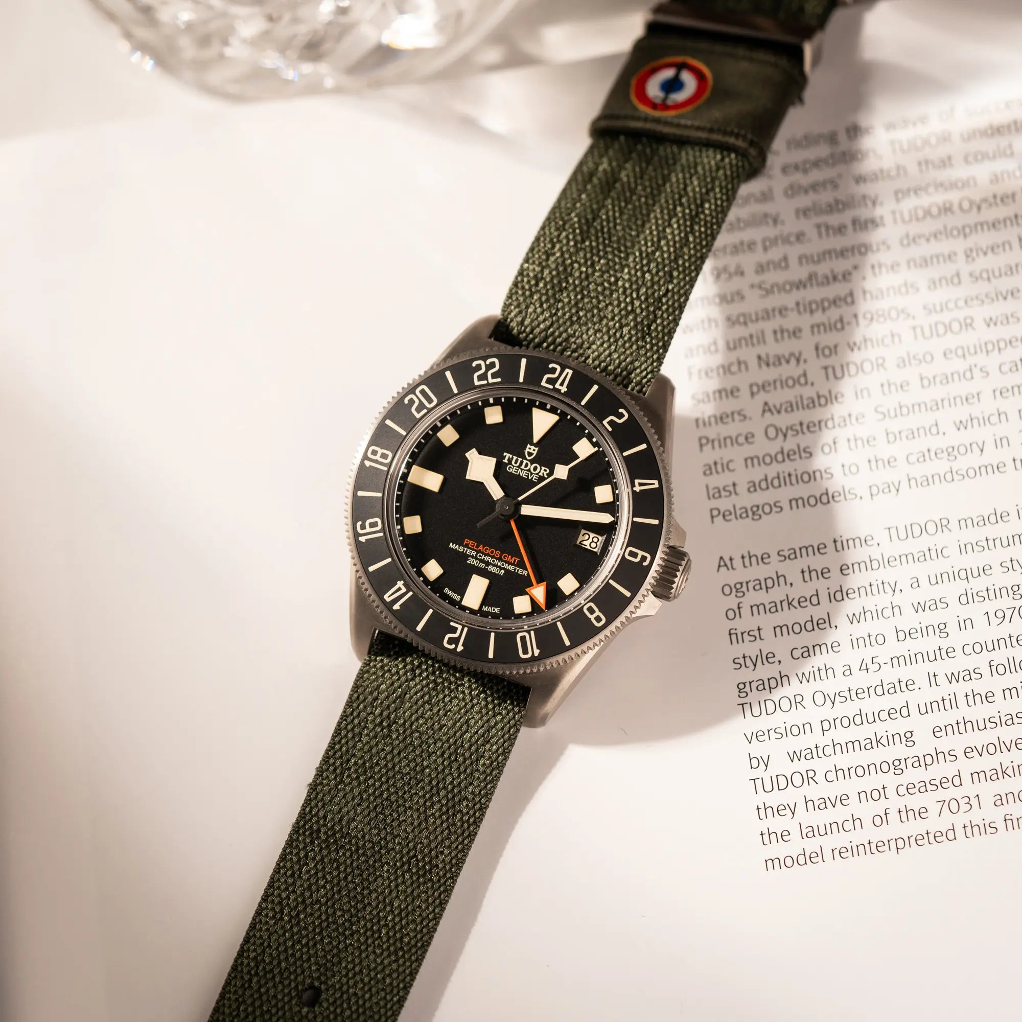 Tudor Pelagos GMT Military der Referenz M2542G257NU-0002 mit Titan-Gehäuse und schwarzem Zifferblatt an einem olivgrünen Nato-Strap liegt auf einem Buch über Tudor-Uhren