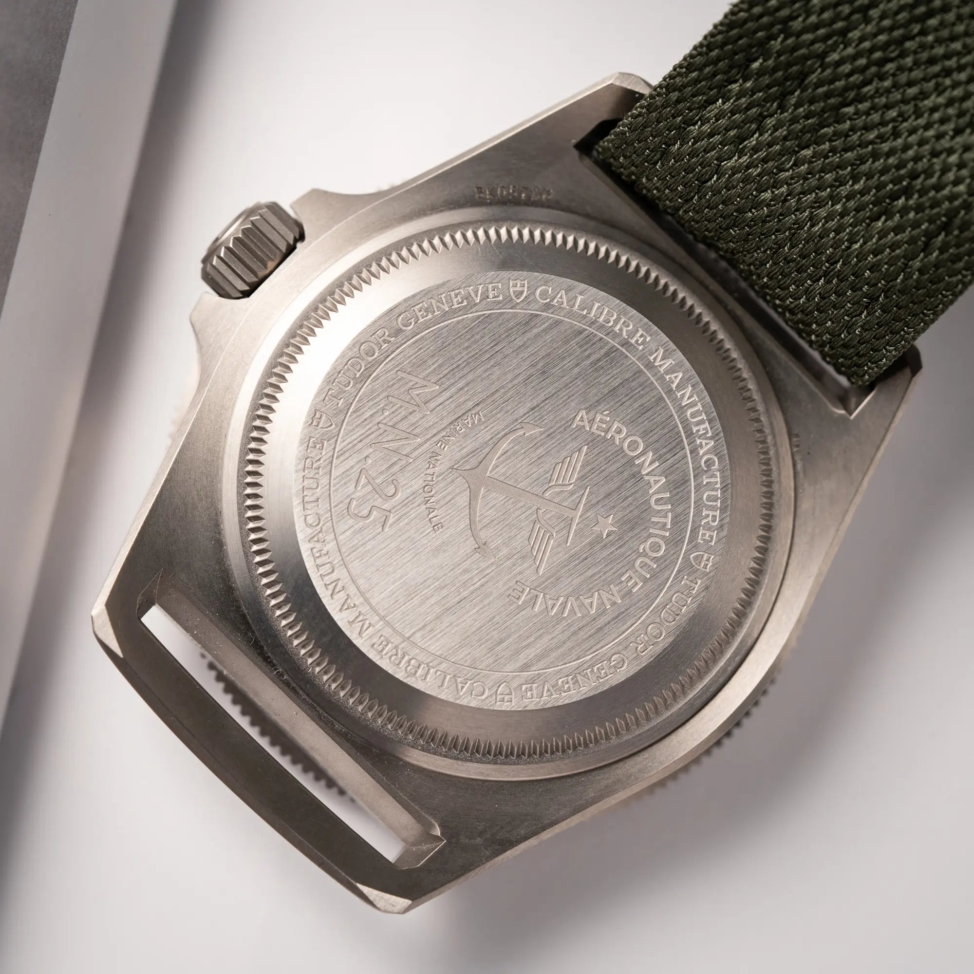 Produktfotografie der Tudor Pelagos GMT Military der Referenz M2542G257NU-0002 mit Titan-Gehäuse und schwarzem Zifferblatt an einem olivgrünen Nato-Strap zeigt die Gravur "Aeronautique Navale" im Gehäuseboden