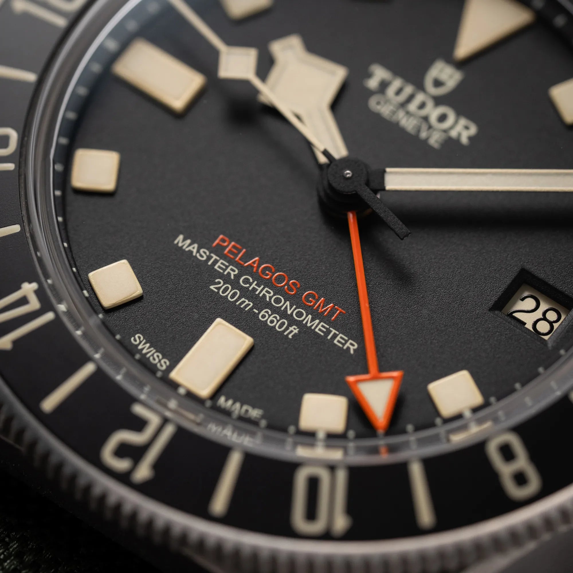 Nahaufnahme der Tudor Pelagos GMT Military der Referenz M2542G257NU-0002 mit Titan-Gehäuse und schwarzem Zifferblatt an einem olivgrünen Nato-Strap mit Fokus auf dem orangefarbenen GMT-Zeiger und dem orangenen "Pelagos GMT" Schriftzug