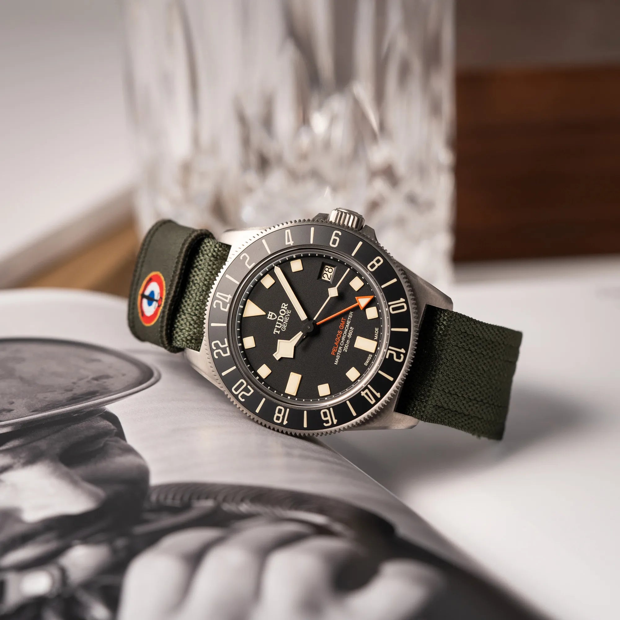 Produktfotografie der seitlich auf dem Uhrengehäuse liegenden Tudor Pelagos GMT Military der Referenz M2542G257NU-0002 mit Titan-Gehäuse und schwarzem Zifferblatt an einem olivgrünen Nato-Strap