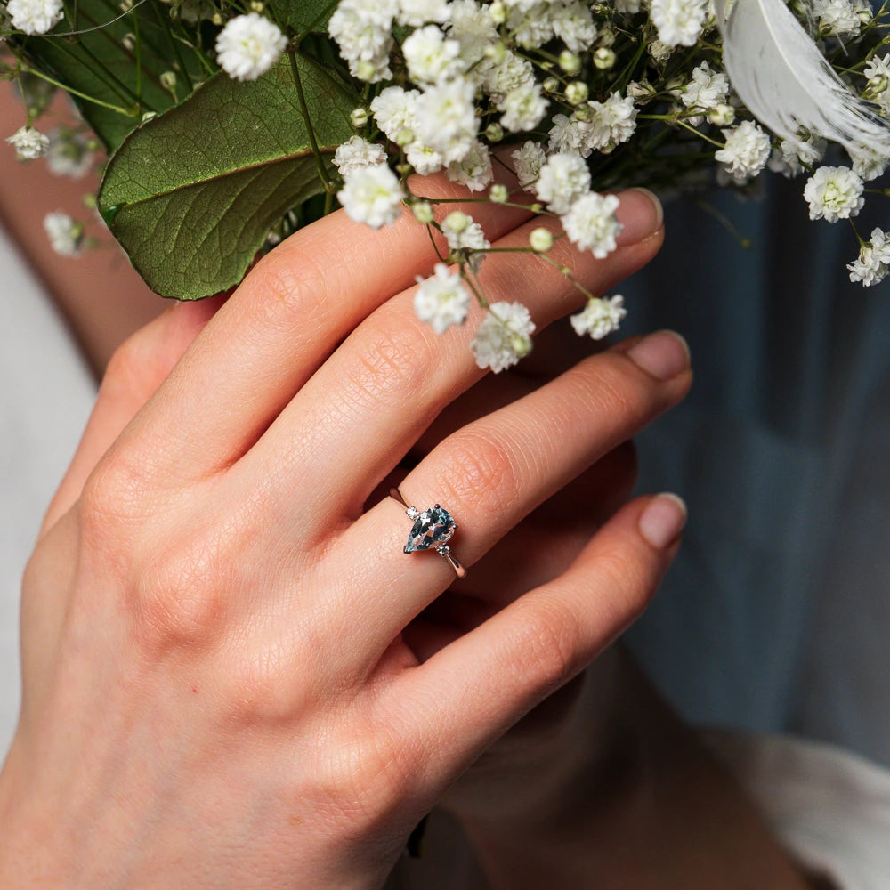 Frau trägt einen Verlobungsring aus Weißgold mit einem Tansanit in Tropfenform an Ihrem Ringfinger, während sie einen Brautstrauß hält