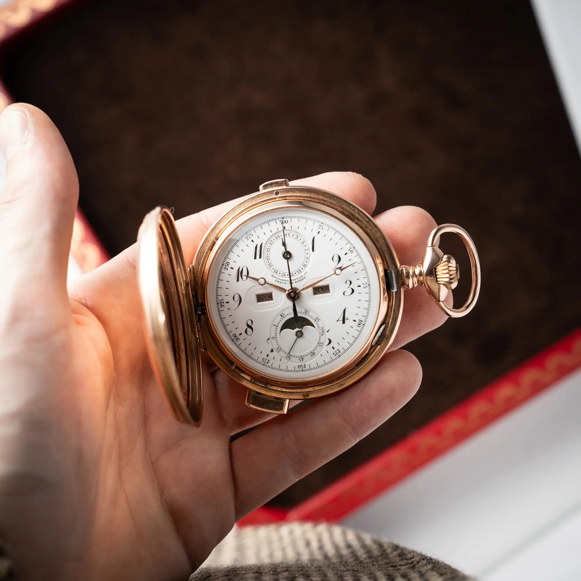 Vollkalender Taschenuhr aus 14 Karat Roségold mit viertel Stunden Repetition und Mondphase-Anzeige bei 6 Uhr auf dem weißen Zifferblatt in einer Männerhand