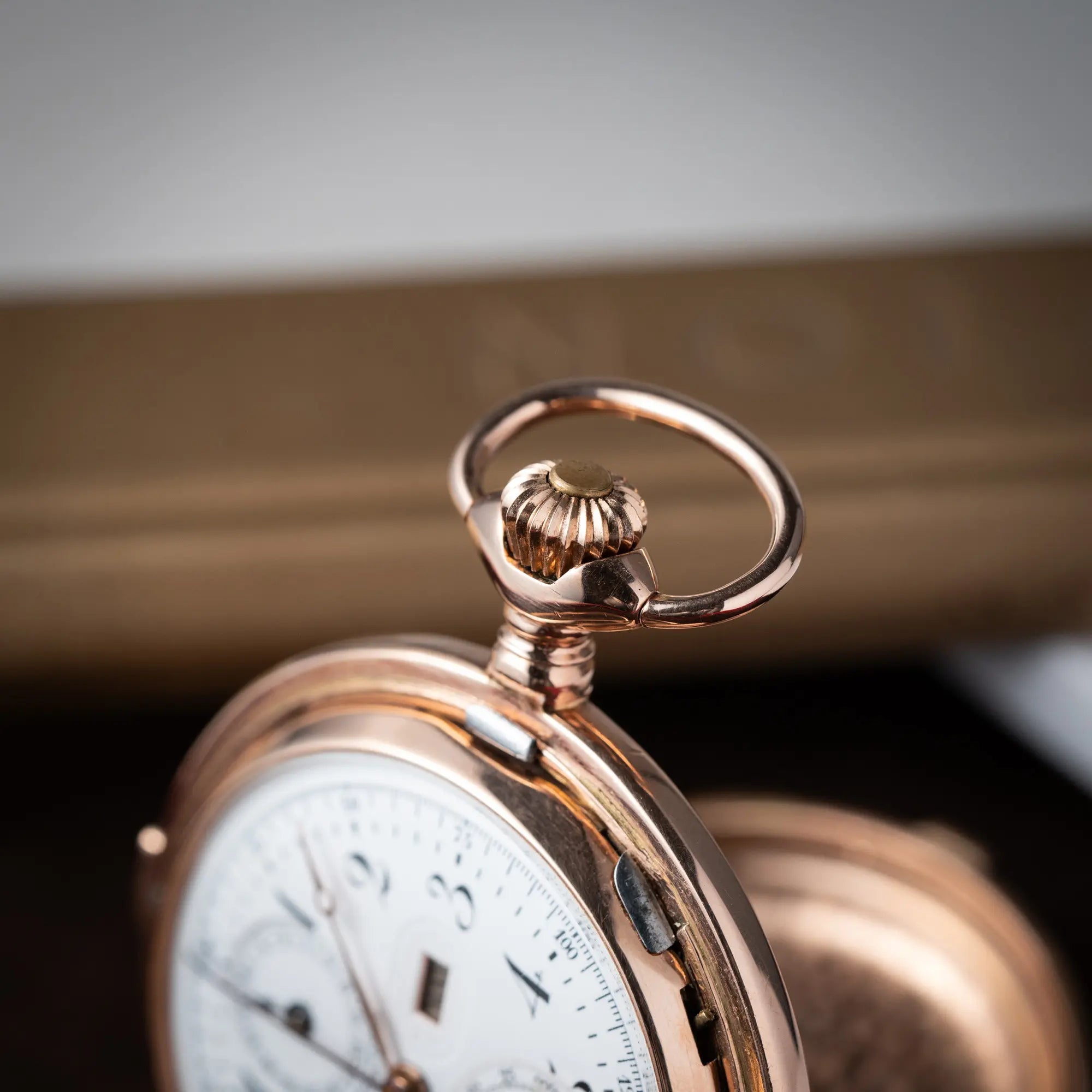 Produktfotografie zeigt die Aufzugskrone von der Vollkalender Taschenuhr aus 14 Karat Roségold mit viertel Stunden Repetition und Mondphase-Anzeige bei 6 Uhr