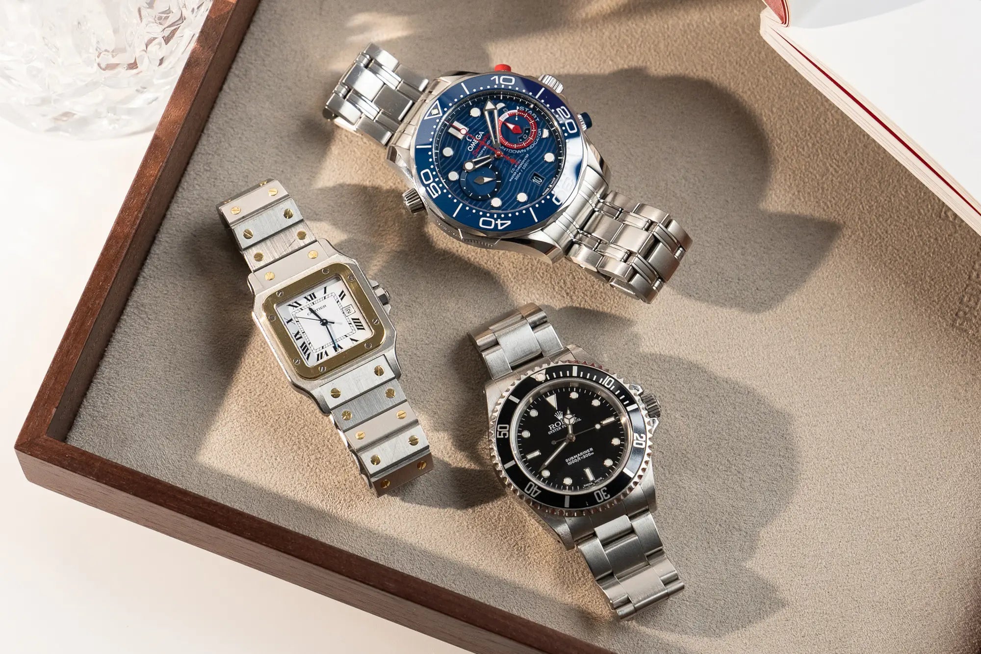 Auswahl an exklusiven Luxusuhren auf einen Juwelierstablet bei Schmuckatelier Lang am Beispiel einer Cartier Santos, Rolex Submariner und eine Omega