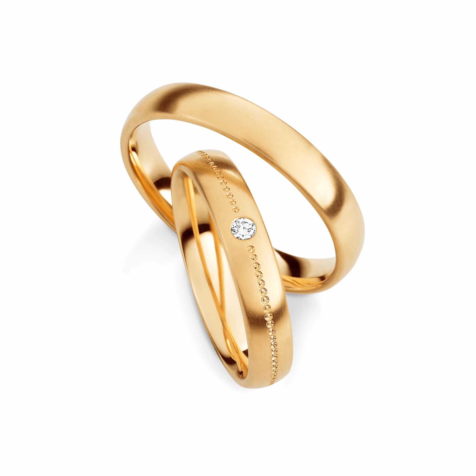 Produktfotografie des gelbgoldenen Max Kemper Trauringpaars mit einer zentralen Linie aud punktartigen Details und einem Diamant als Highlight im Dqmenring
