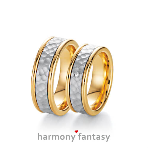Produktfotografie des Trauringpaars Harmony Fantasy in Gelbgold mit eingesetztem Weißgold-Streifen in Hammerschlag-OptikWeißgold, mit einem Diamant im Damenring