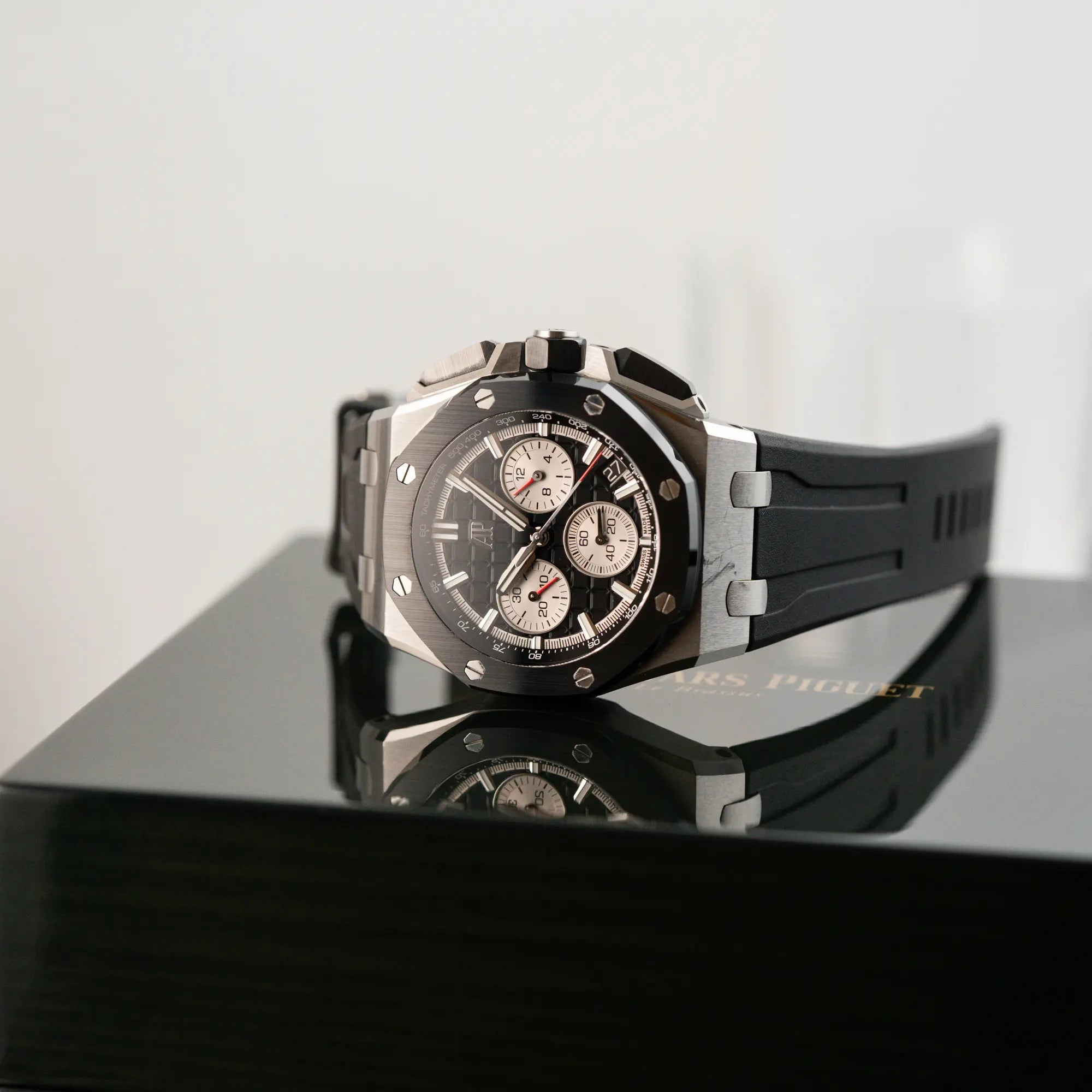 Produktfotografie des Audemars Piguet Royal Oak Chronograph 26420SO.OO.A002CA.01 mit schwarzem Zifferblatt und Lünette, während die Uhr auf der originalen Uhrenbox liegt