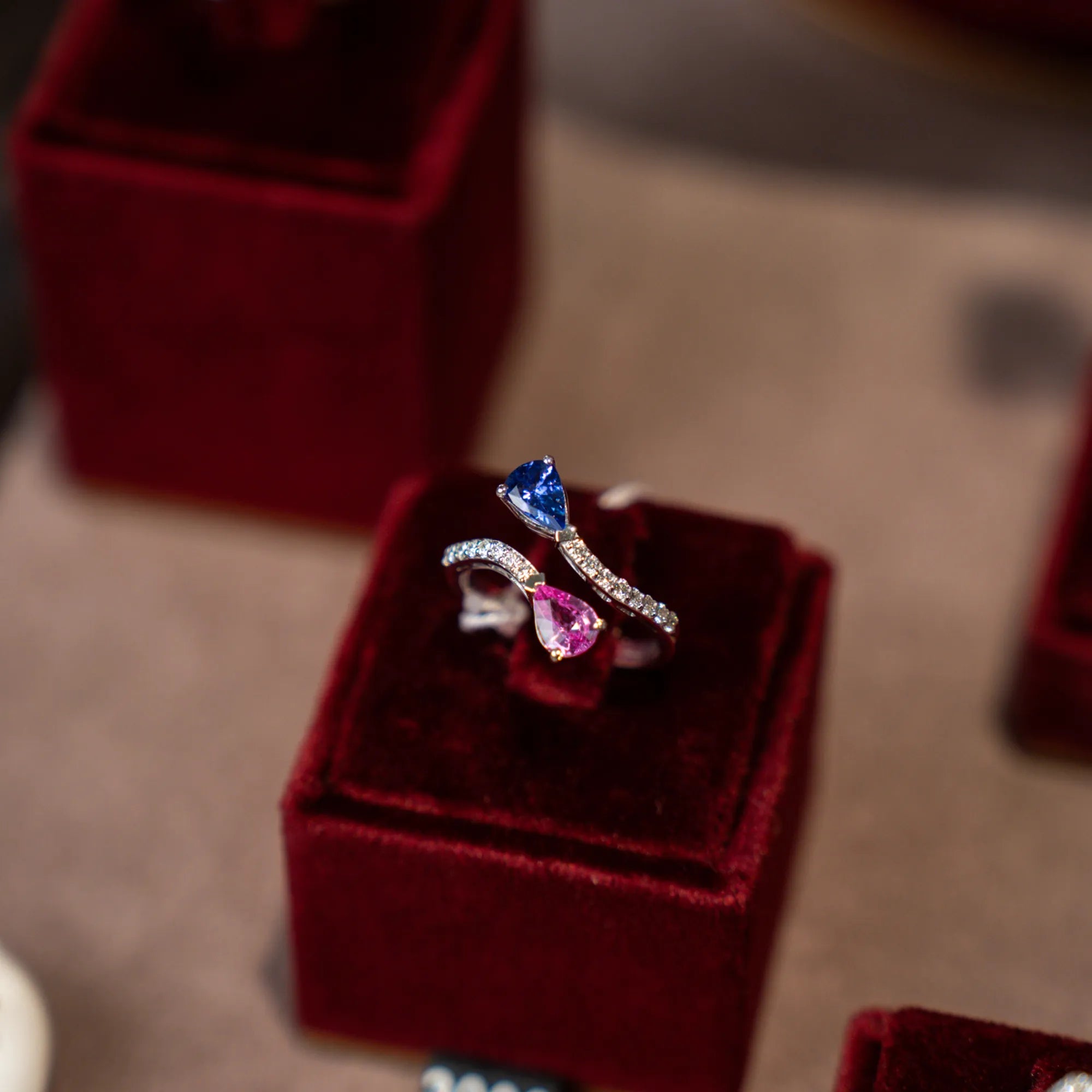 Produktfotografie des Rings ATZRC-59 von Lunatica Roma aus Weissgold mit einer offenen, diamantbesetzten Ringschiene, die jeweils mit einem rosa Saphir im Tropfenschliff und einem blauen Tansanit abschliessen