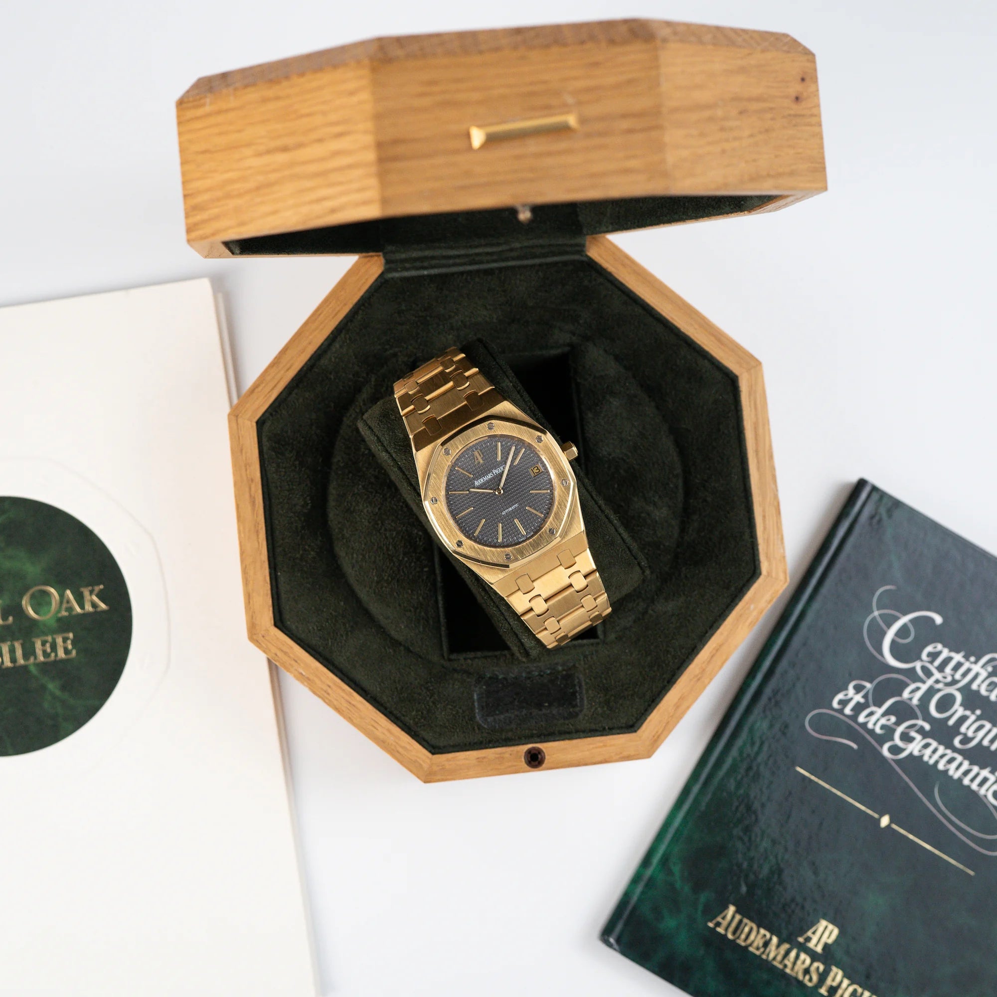 Audemars Piguet Royal Oak Jumbo 14802BA Jubilee in Gelbgold liegt in der Uhrenbox aus Holz und daneben liegt der Lieferumfang, bestehend aus Zertifikat und Booklet