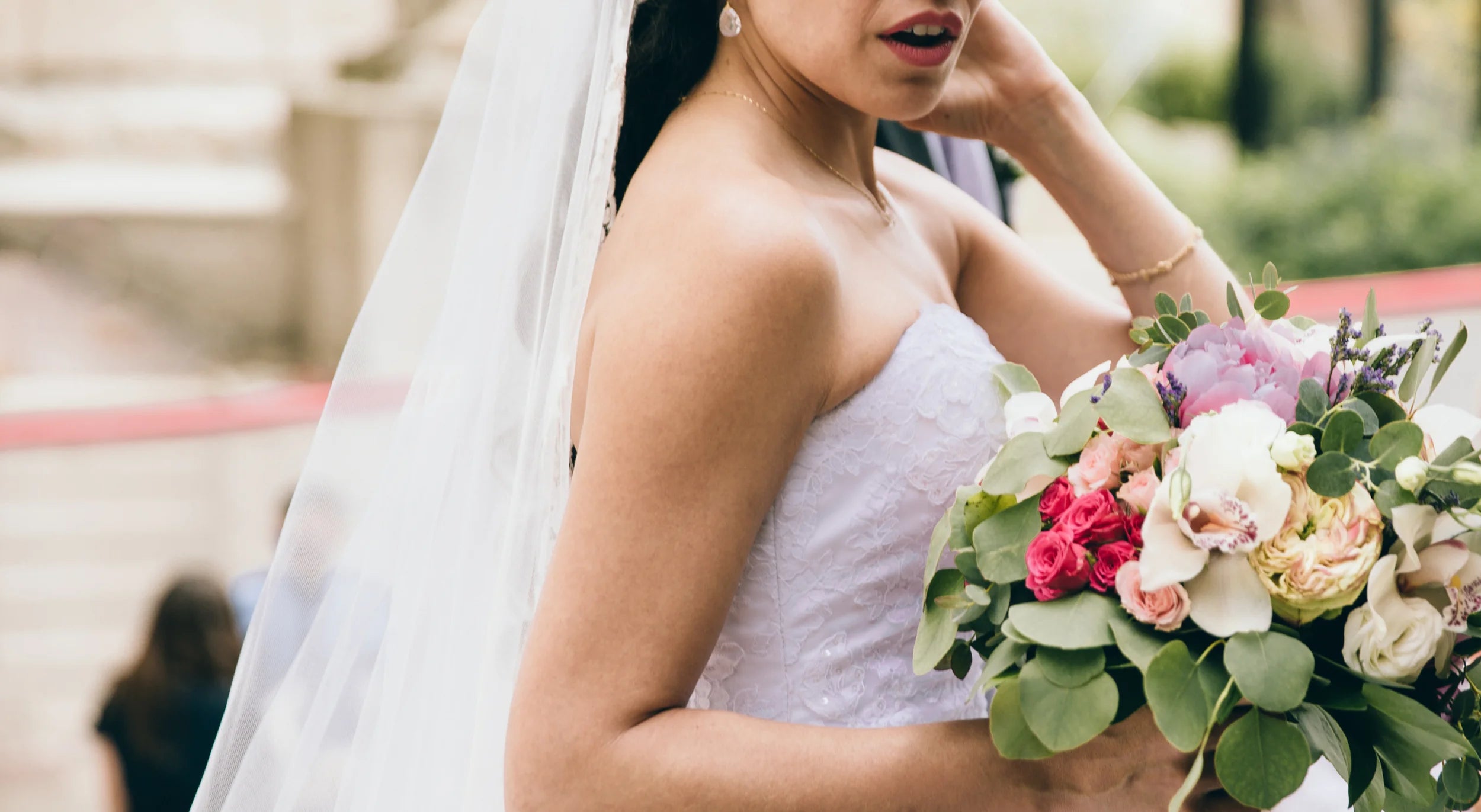 Braut im Hochzeitskleid hält Ihren Brautstrauß in der Hand