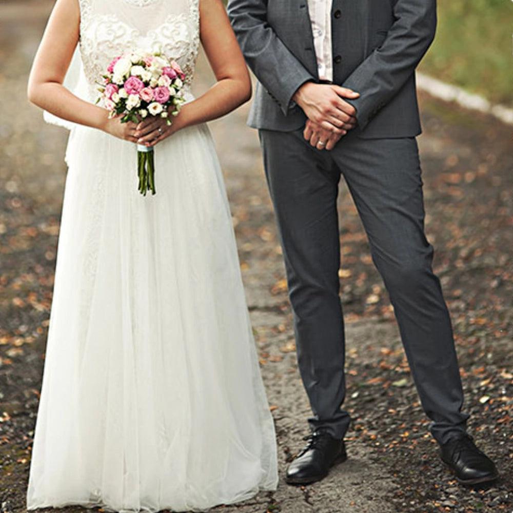 Brautpaar posiert am Hochzeitstag in Hochzeitskleid und im Anzug während die Braut ihren Brautstrauß hält