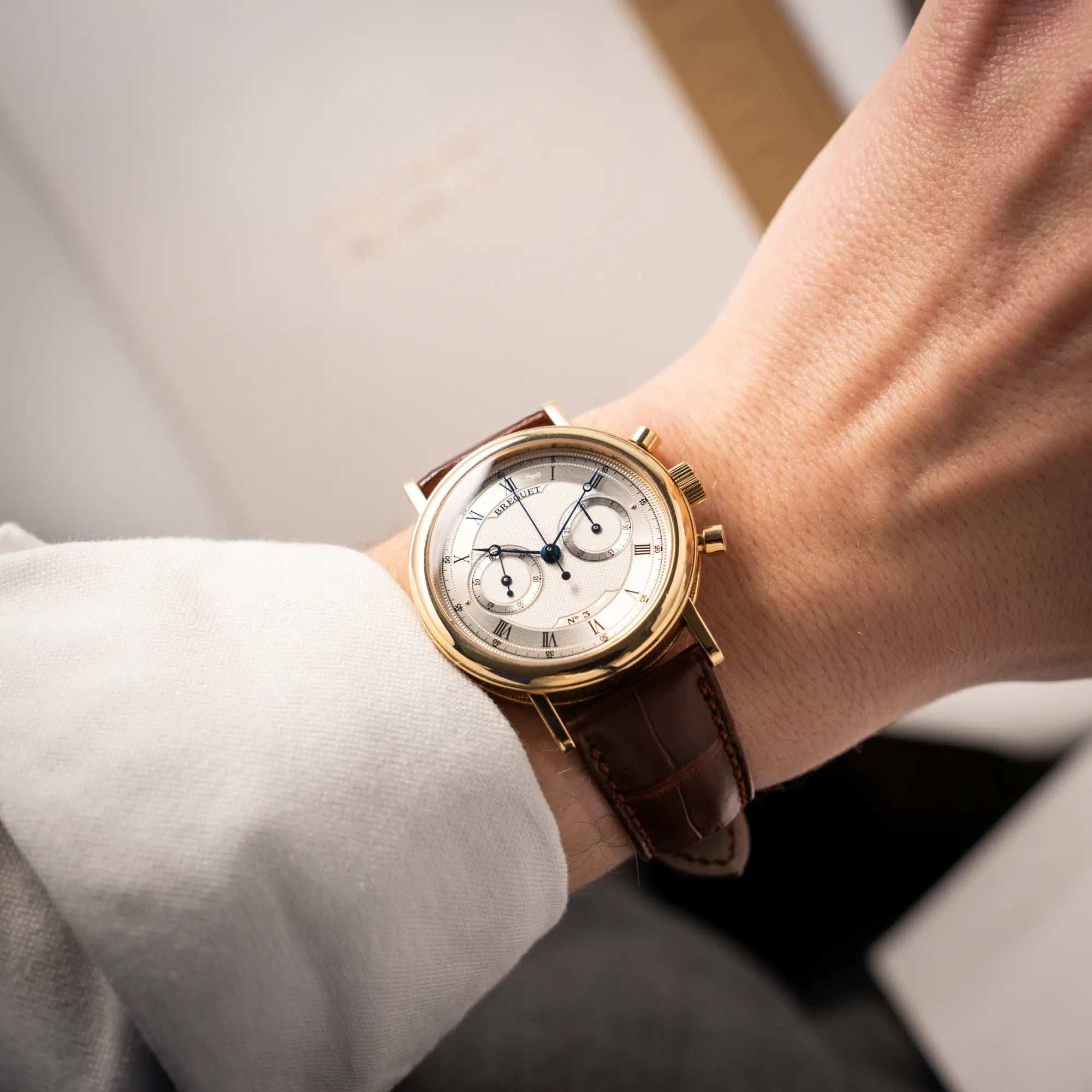 Mann trägt den Breguet Classique Chronograph der Referenz 5237 in Gelbgold mit silbernem guillochiertem Zifferblatt am braunem Lederband an seinem Handgelenk