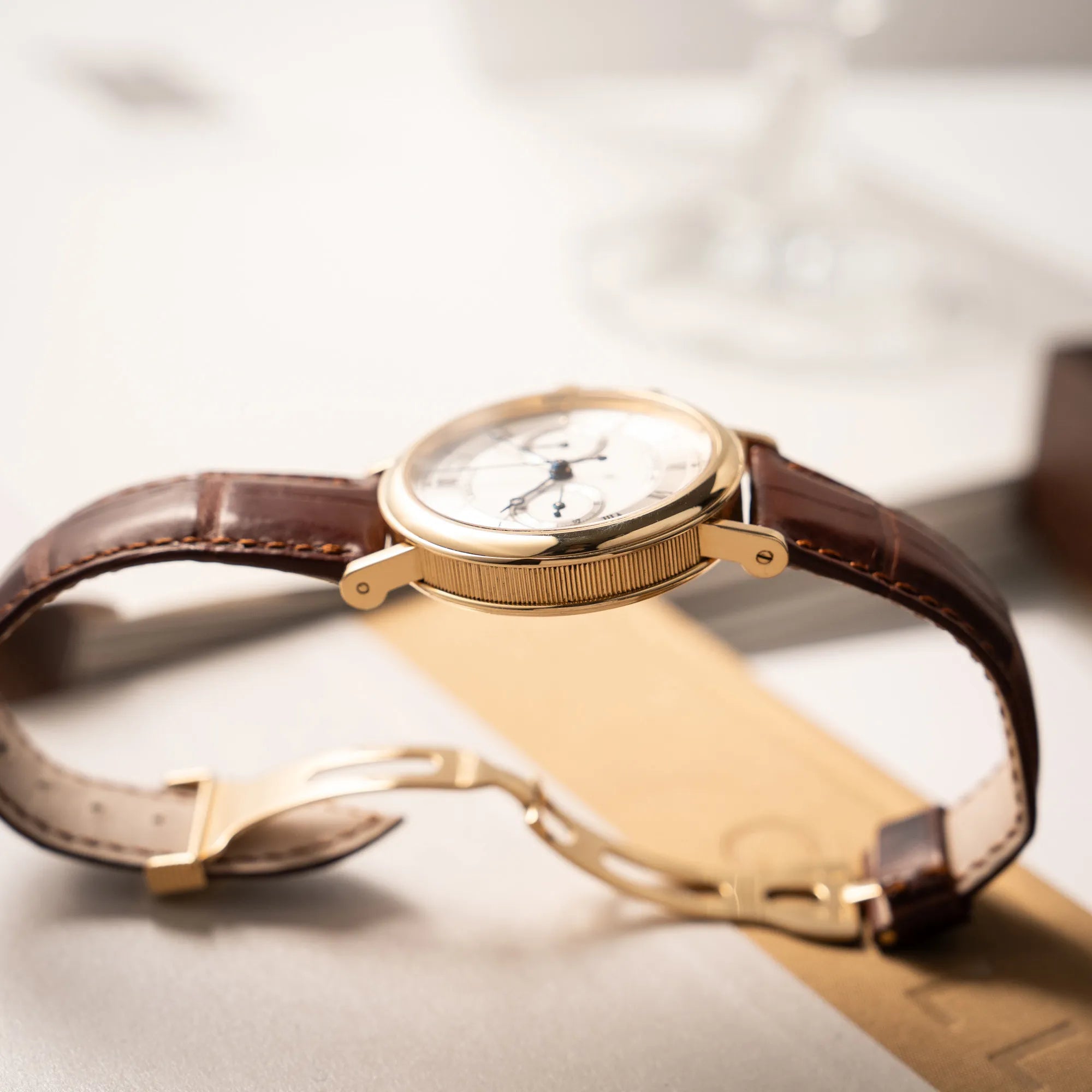 Produktfotografie ds Breguet Classique Chronograph der Referenz 5237 in Gelbgold mit silbernem guillochiertem Zifferblatt am braunem Lederband  zeigt die kannelierte Gehäusflanke der Armbanduhr