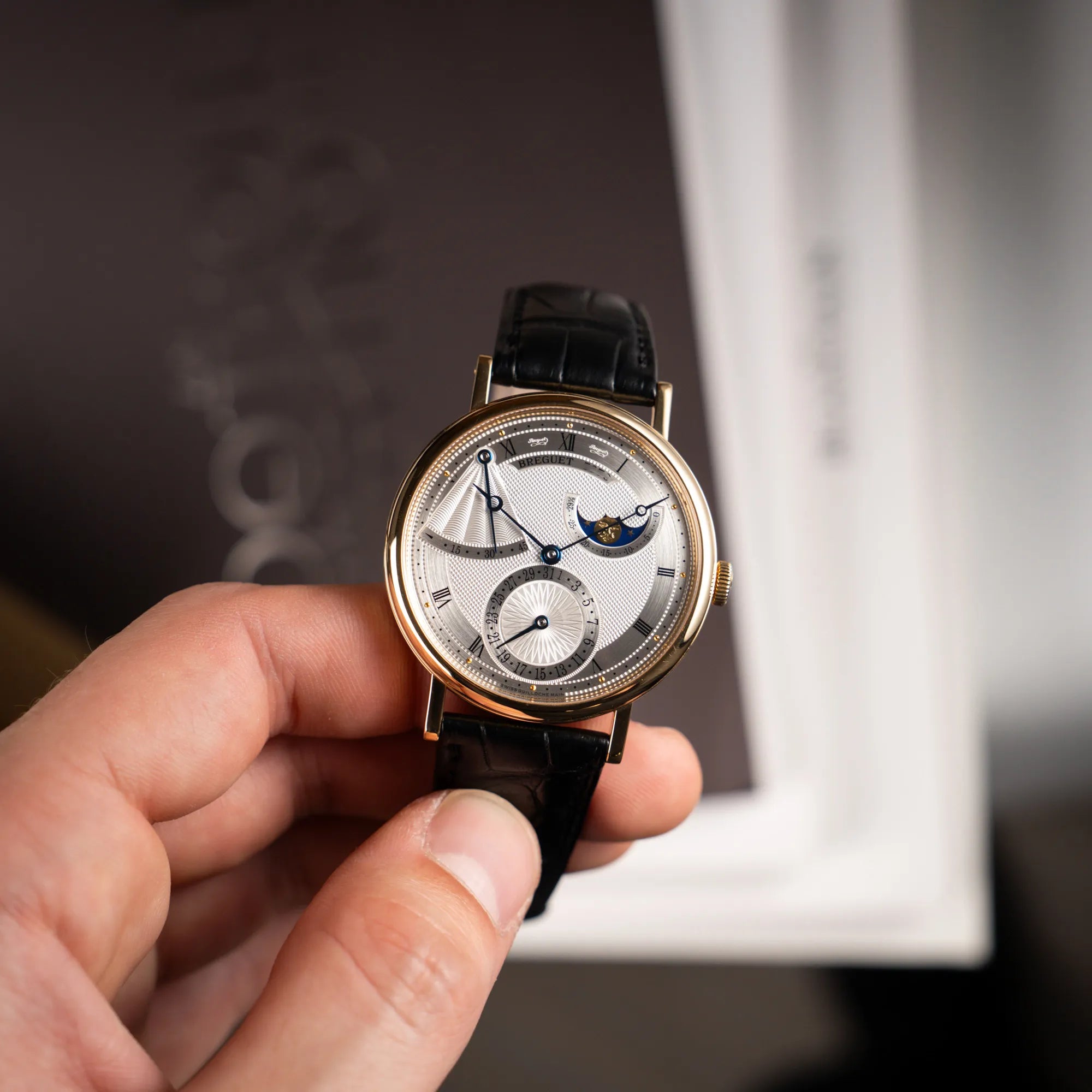 Mann hält die  Breguet Classique Mondphase 7137 in Gelbgold mit silbernen, verschieden guillochiertem Zifferblatt und präsentiert die Uhr in die Kamera