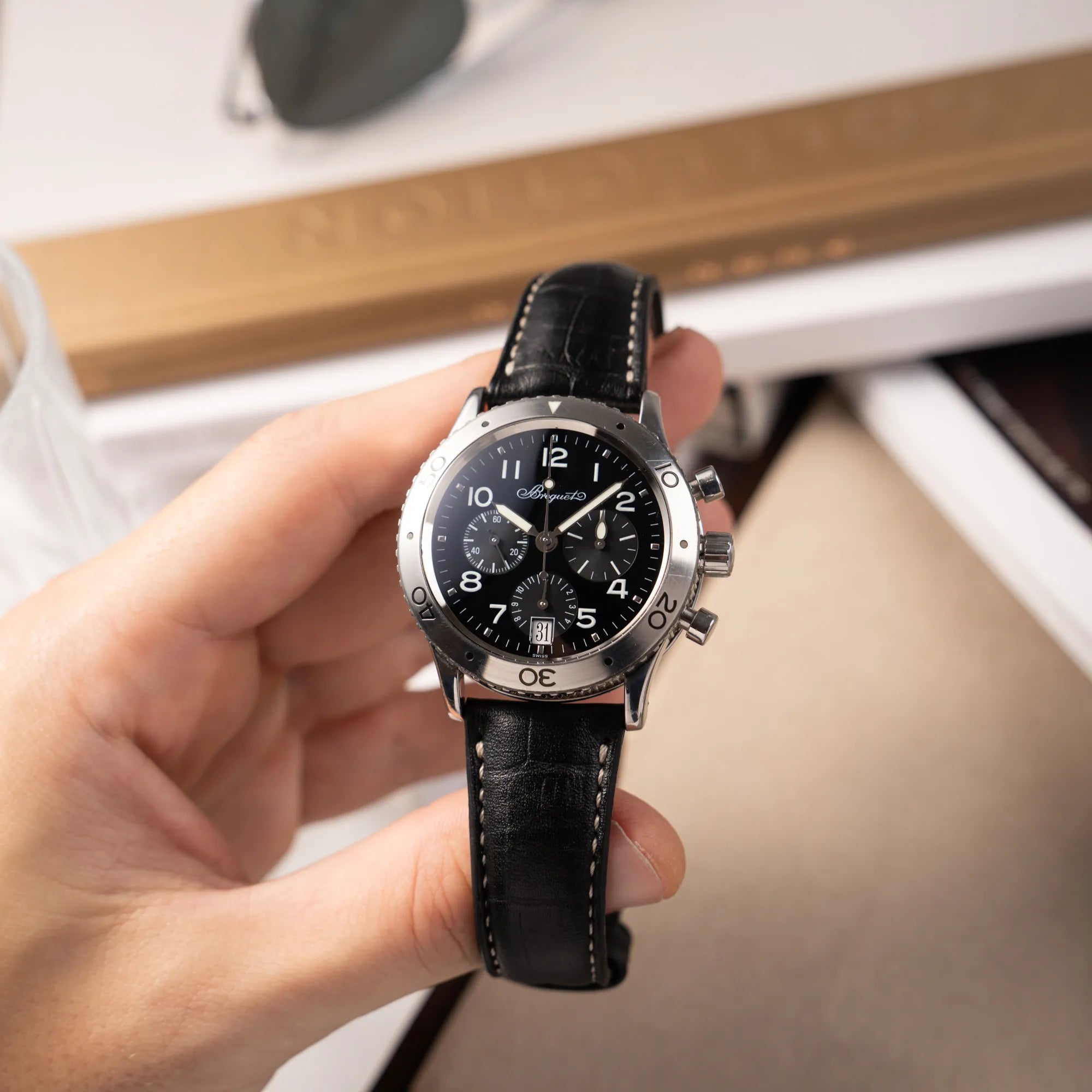 Mann hält die Breguet Type XX Aéronavale Transatlantique der Referenz 3820ST mit schwarzem Lack-Zifferblatt am originalen schwarzen Breguet-Lederband in seiner Hand und präsentiert die Uhr in die Kamera