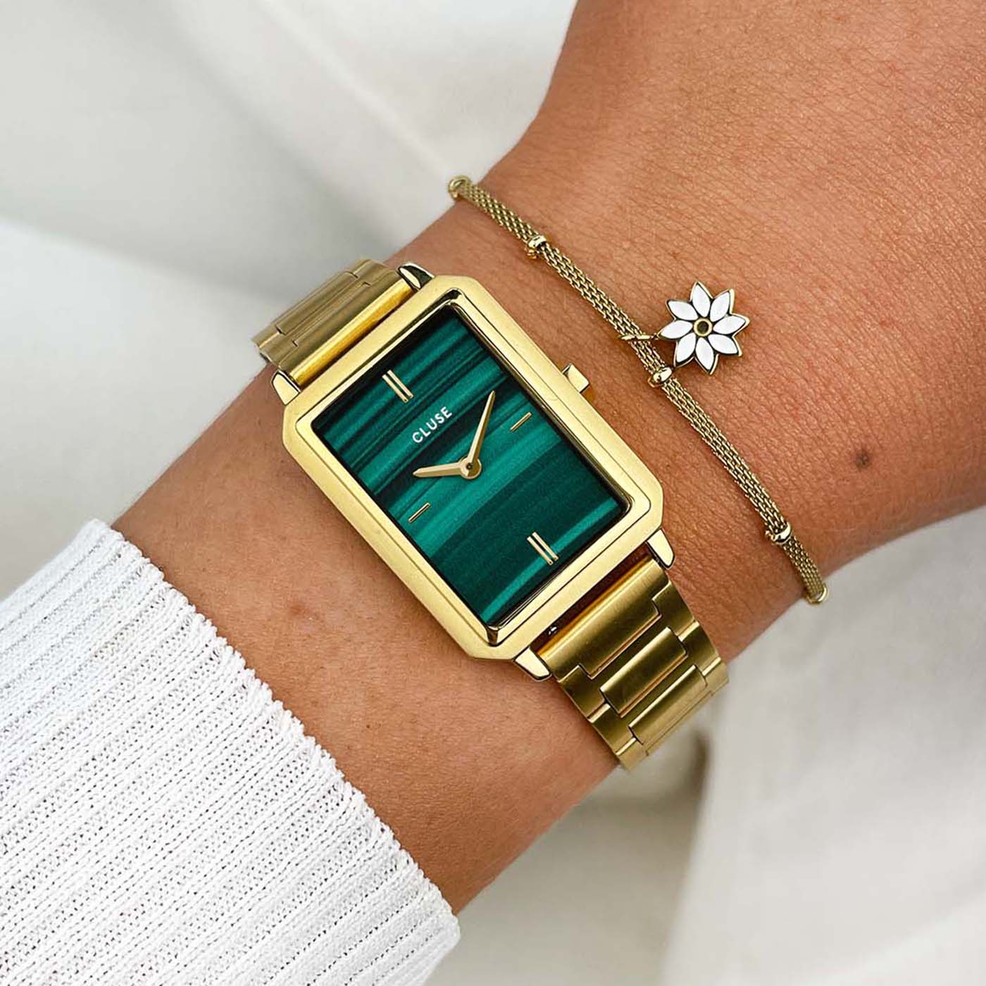 Frau trägt die Cluse "Fluette" Stahl-Uhr mit grünem Malachit-Druck-Zifferblatt mit goldfarbenem Gehäuse und kombiniert es mit einem goldenen Armband