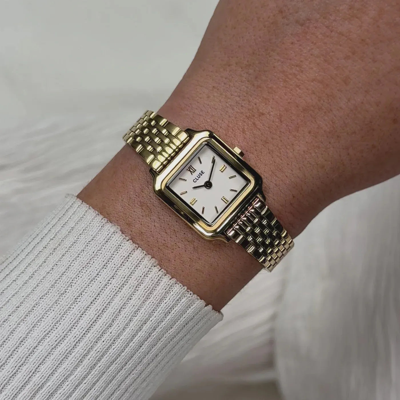 Frau trägt die goldfarbene Cluse Gracieuse Mini CW15506 Damenuhr mit weißem Zifferblatt an ihrem Handgelenk