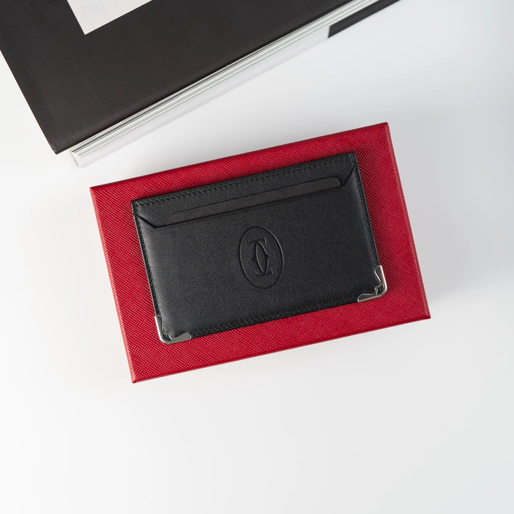 Produktfotografie des schwarzen Cardholders von Cartier aus schwarzem Leder, der auf der roten Umverpackung liegt