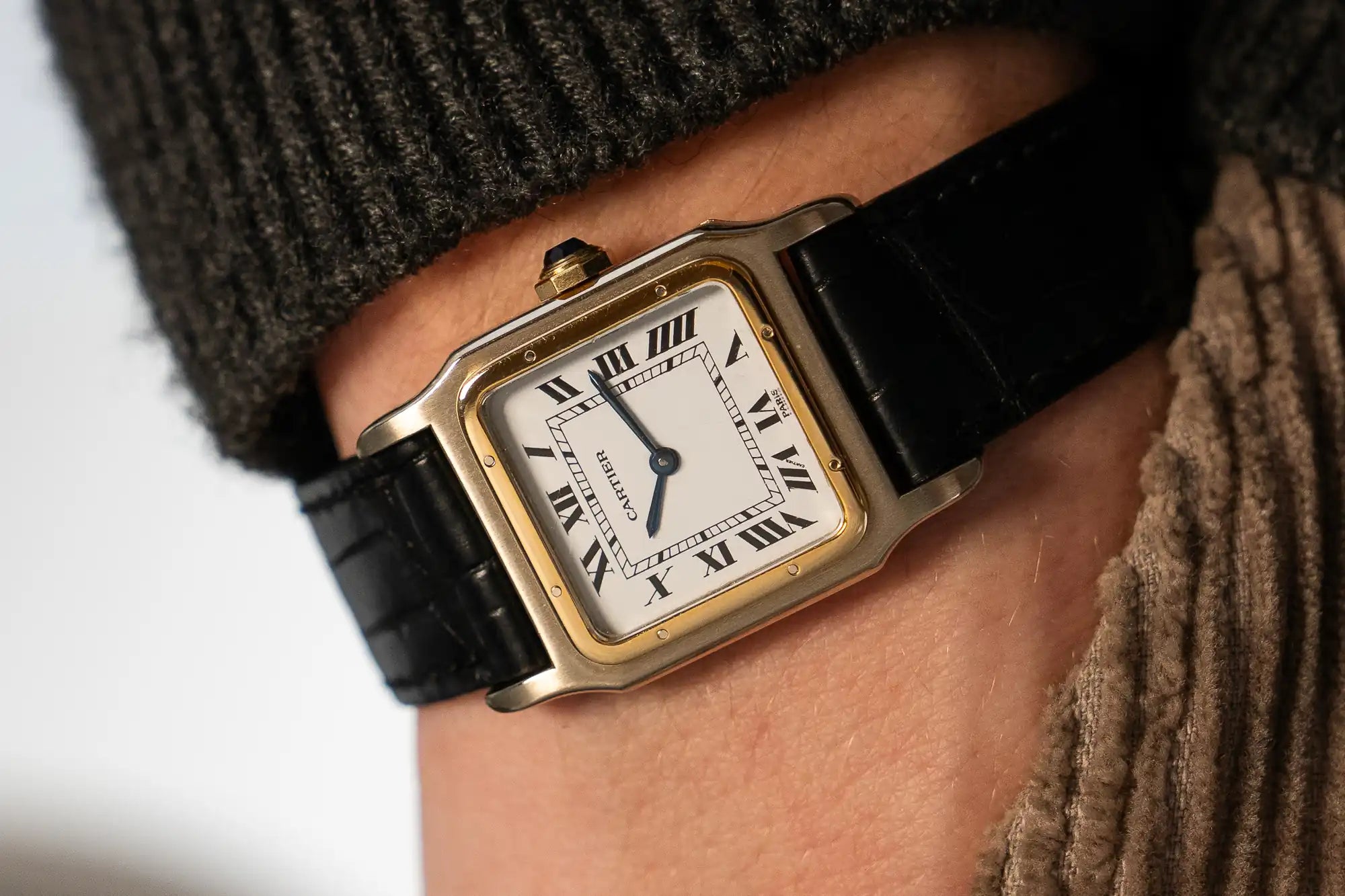 Mann trägt die seltene Cartier Santos Deux Ors mit Paris-Zifferblatt und mit schwarzem Lederband an seinem Handgelenk 