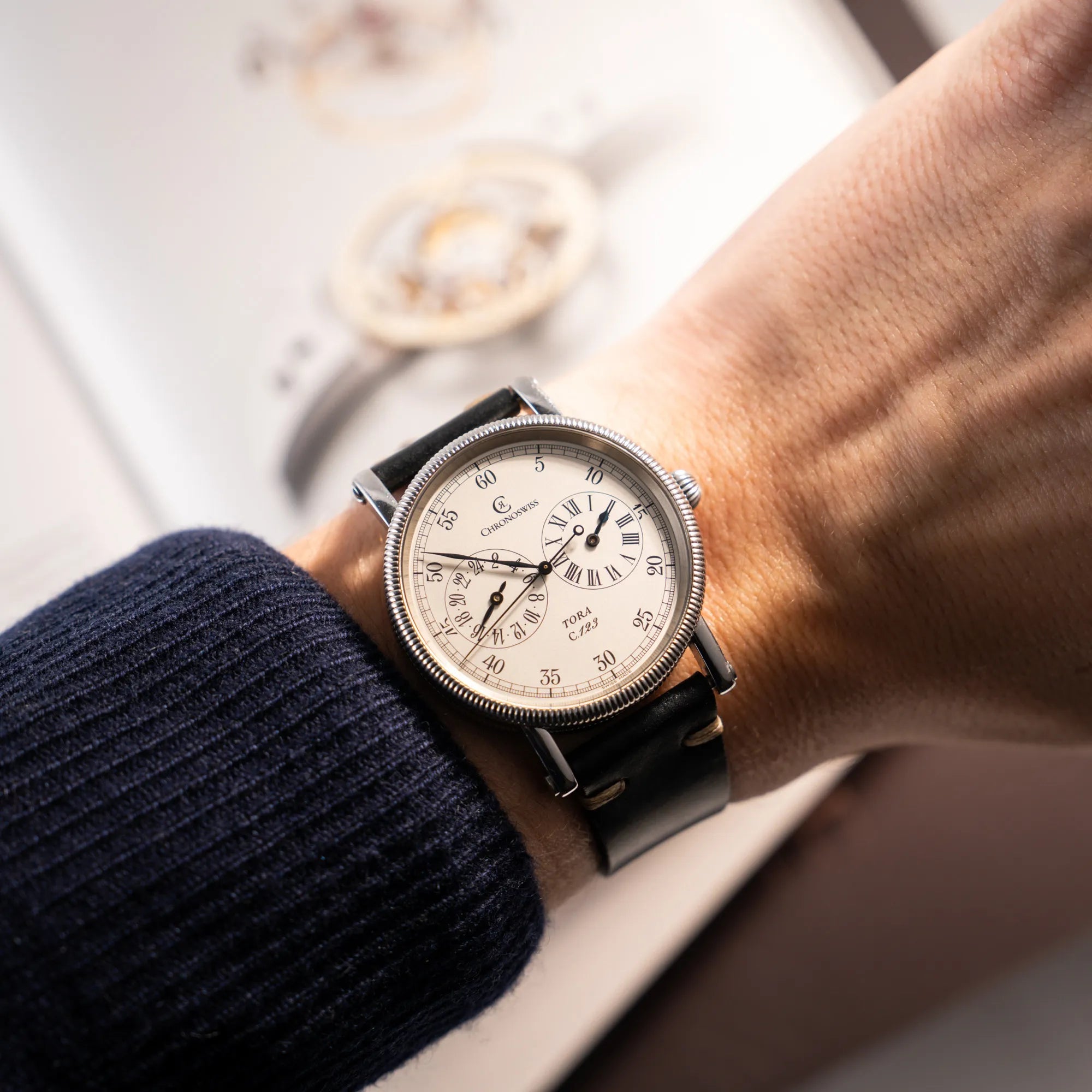 Mann trägt die Chronoswiss Regulator Tora C123 mit weißem Zifferblatt mit zwei symmetrisch angeordneten Hilfszifferblättern mit römischen Indizes an seinem Handgelenk