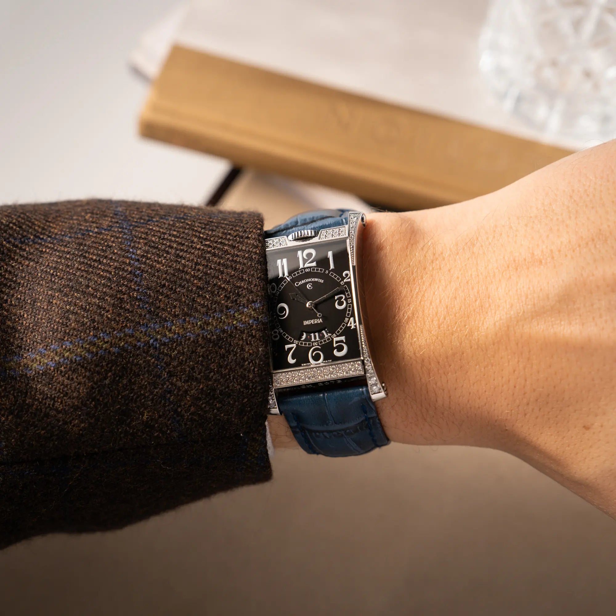 Mann trägt die Chronoswiss Imperia Constanze mit diamantbesetzten-Stahlgehäuse mit schwarzem Zifferblatt an einem petrol-blauem Lederband