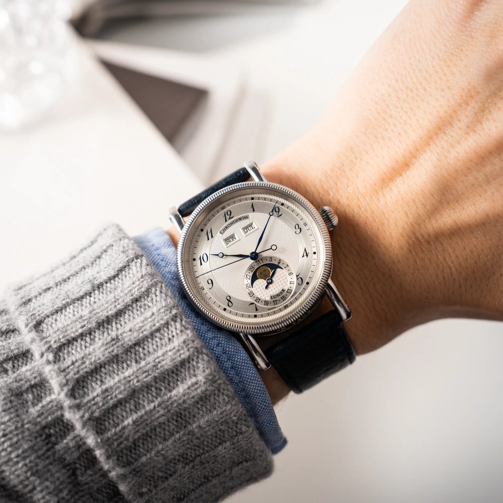 Wristshot mit der Chronoswiss Klassic Luna Mondphase CH9323 mit silbernem, guillochiertem Zifferblatt mit Kalenderanzeige auf 12 Uhr und einer Mondphase-Anzeige bei 6 Uhr