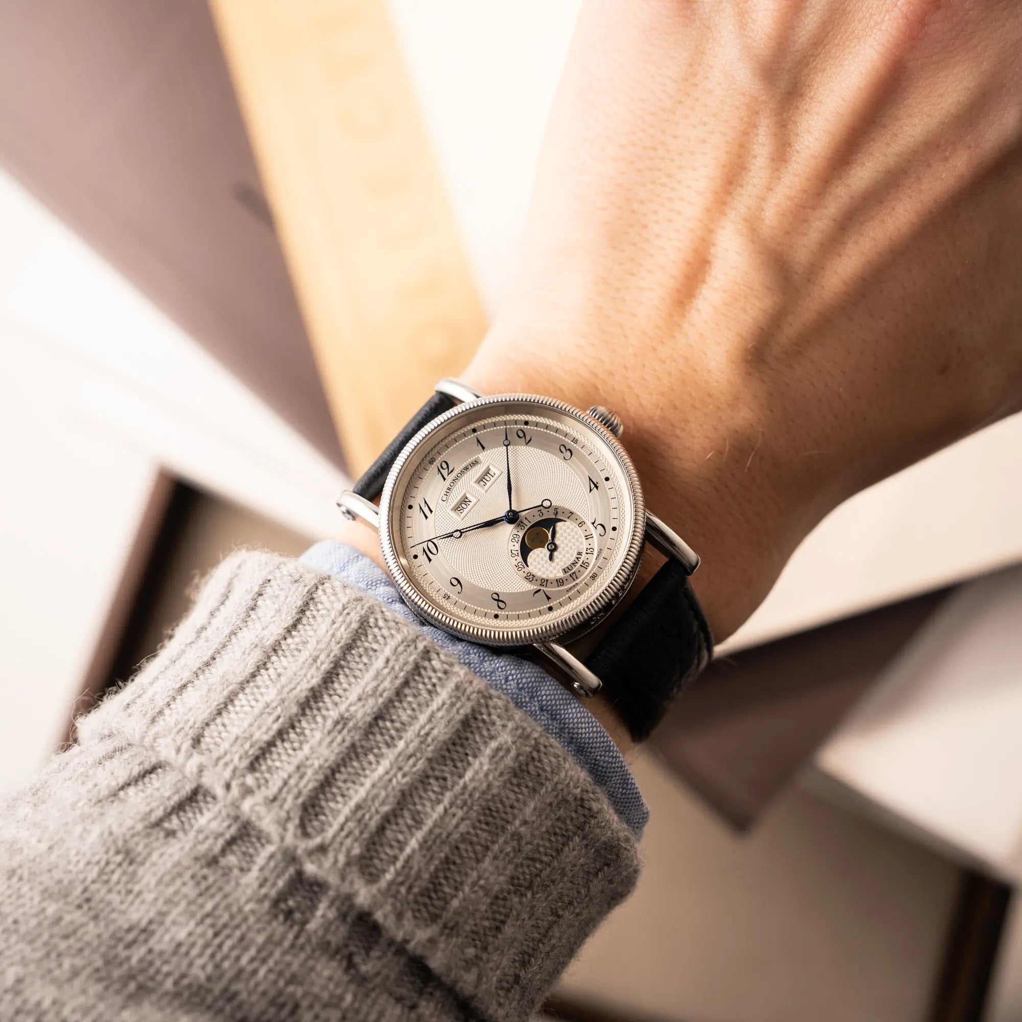 Wristshot mit der Chronoswiss Klassic Luna Mondphase CH9323 mit silbernem, guillochiertem Zifferblatt mit Kalenderanzeige auf 12 Uhr und einer Mondphase-Anzeige bei 6 Uhr