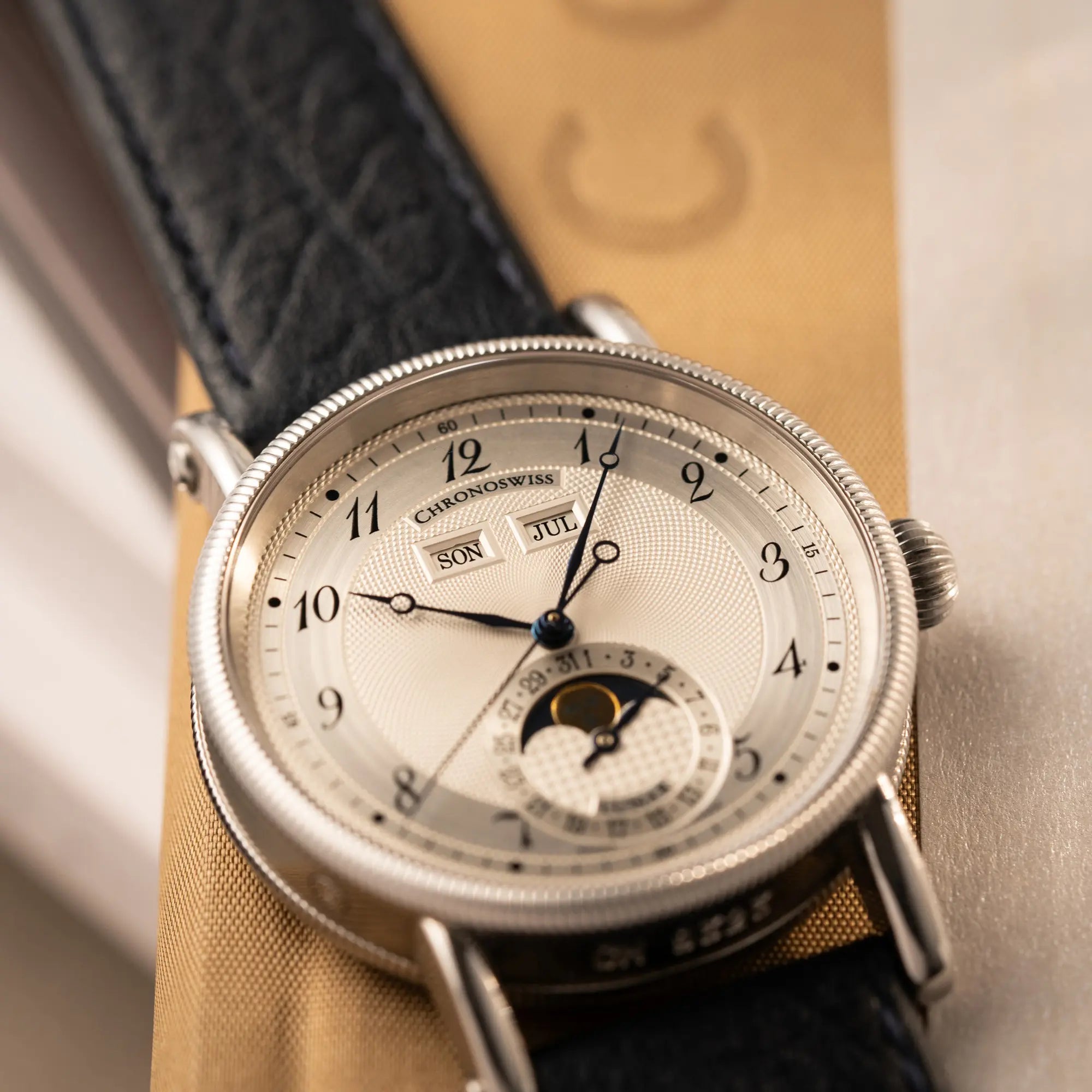 Produktfotografie der Chronoswiss Klassic Luna Mondphase CH9323 mit silbernem, guillochiertem Zifferblatt mit Kalenderanzeige auf 12 Uhr und einer Mondphase-Anzeige bei 6 Uhr mit Fokus auf der Tages und Monatsanzeige