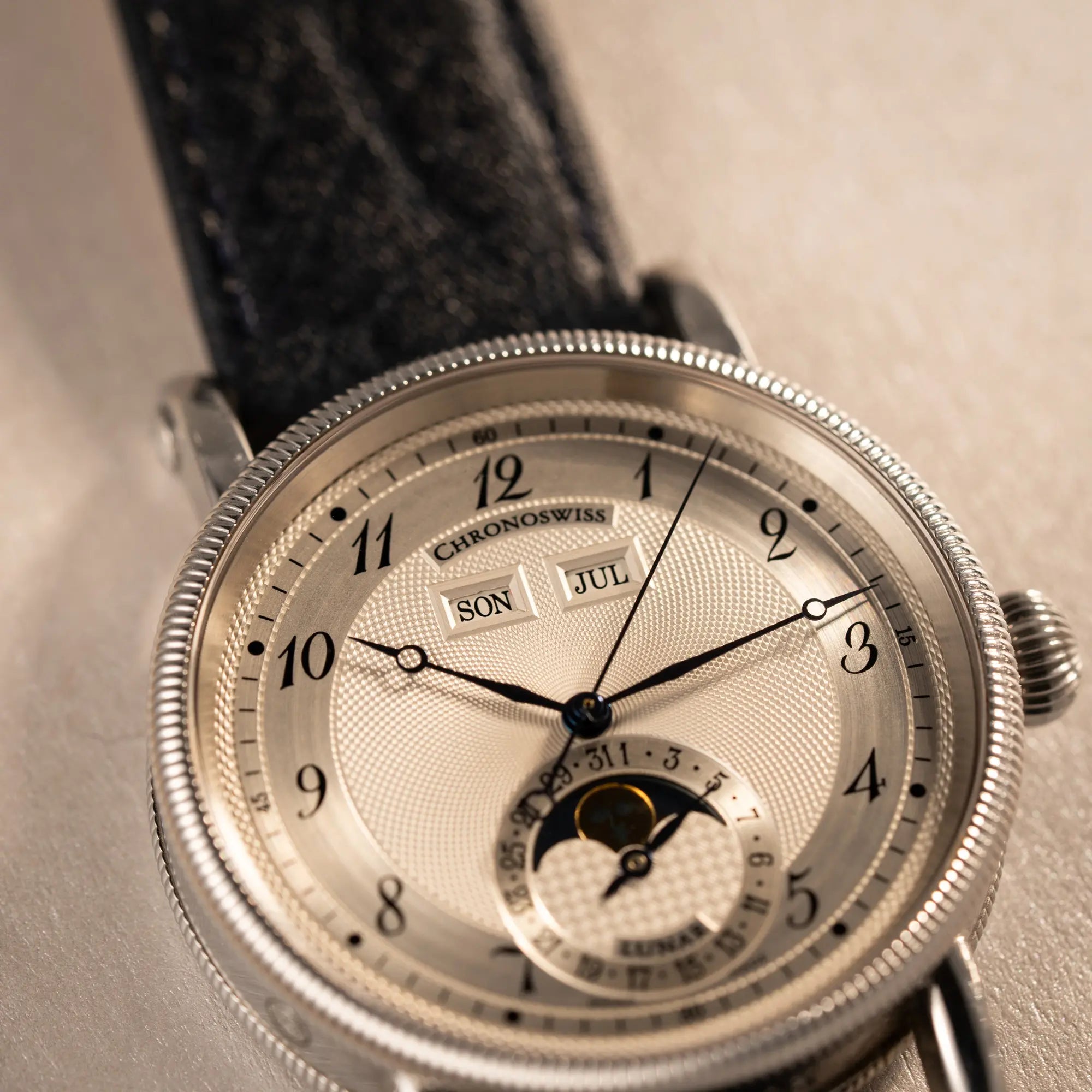 Detailaufnahme der Chronoswiss Klassic Luna Mondphase CH9323 mit silbernem, guillochiertem Zifferblatt mit Kalenderanzeige auf 12 Uhr und einer Mondphase-Anzeige bei 6 Uhr